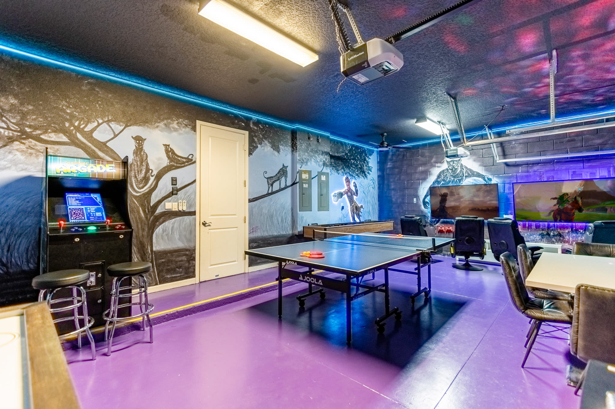 Vibrant game room with a purple floor, featuring a ping pong table, arcade machine, and shuffleboard. The walls are adorned with murals of jungle animals and a large TV setup, illuminated by blue LED strip lighting.