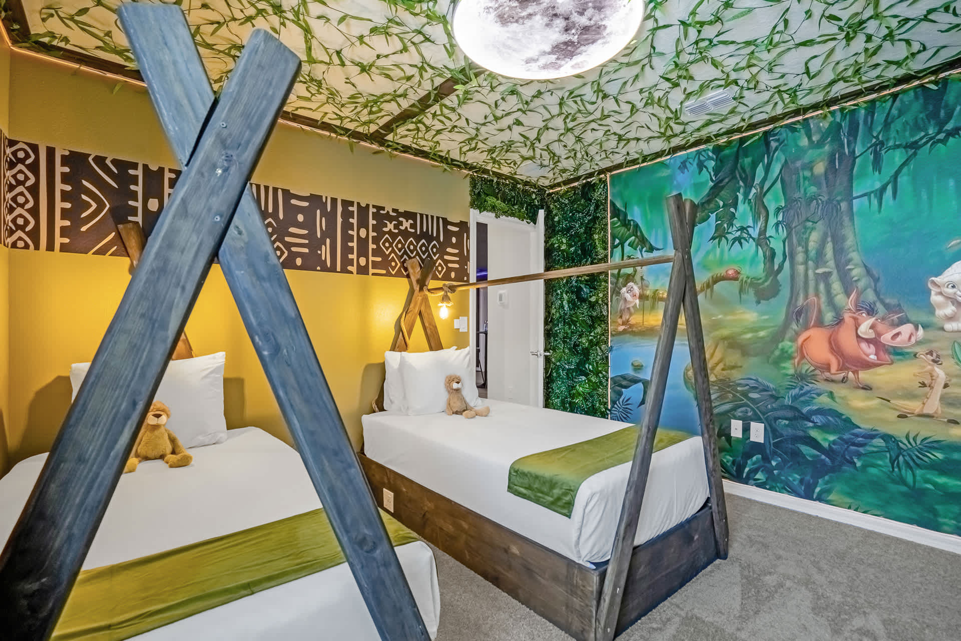 Themed bedroom with two twin beds featuring dark wooden A-frame bed frames, a large mural of jungle characters, and a ceiling covered in artificial vines with a moon-shaped light fixture.