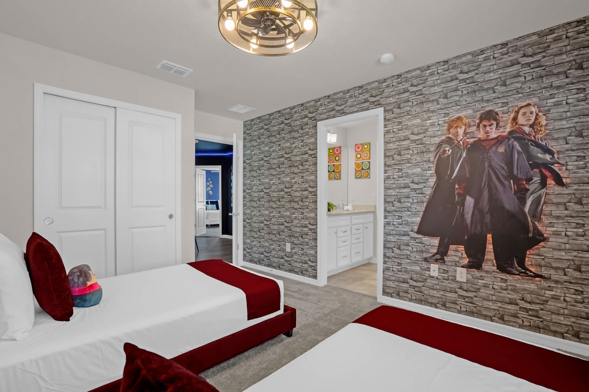 Themed bedroom featuring a large character mural on a stone-patterned wall, two red velvet twin beds, and a doorway leading to an en-suite bathroom.