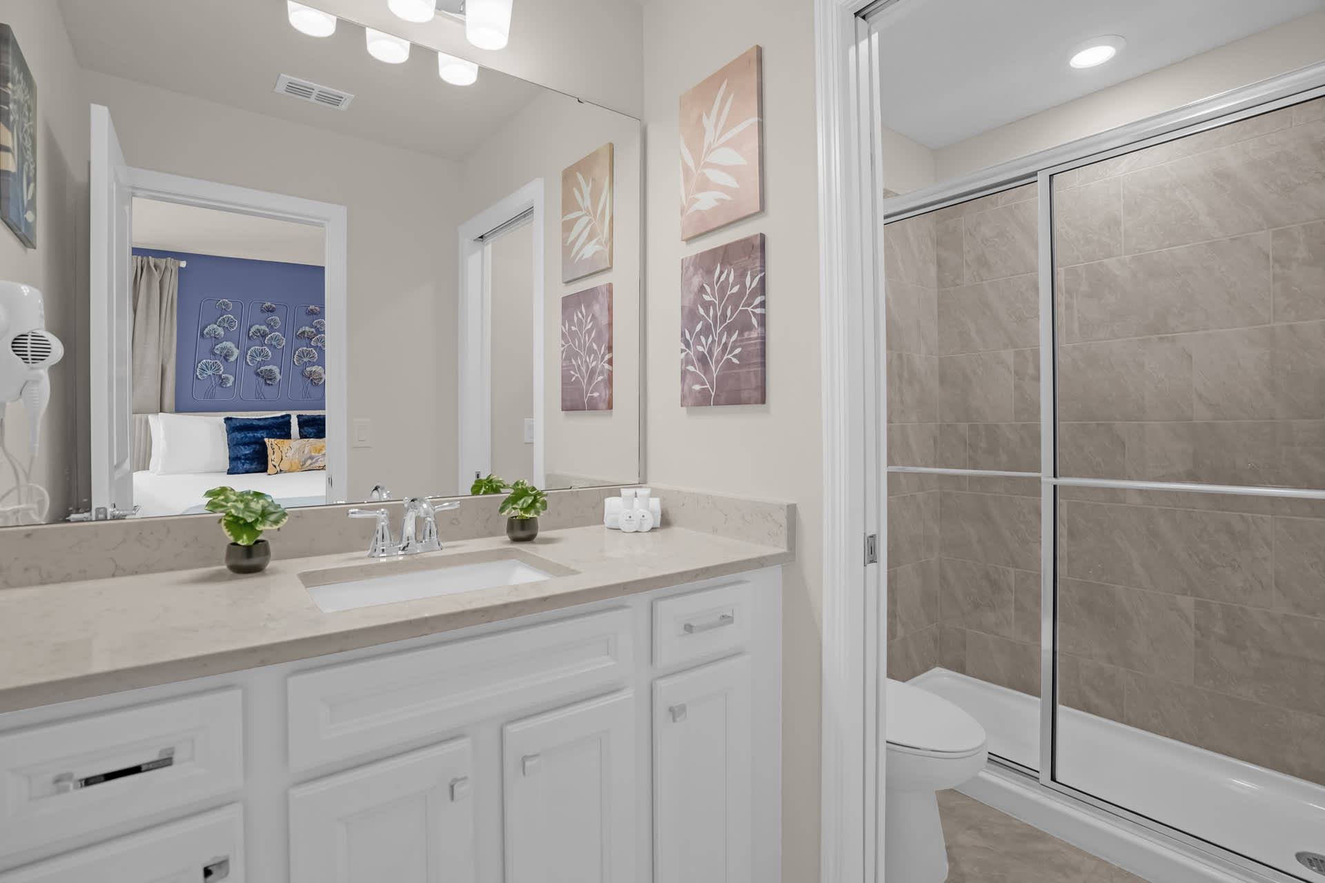 Contemporary bathroom with a single vanity featuring white cabinets, a light countertop, a large mirror, and a walk-in shower with a sliding glass door.
