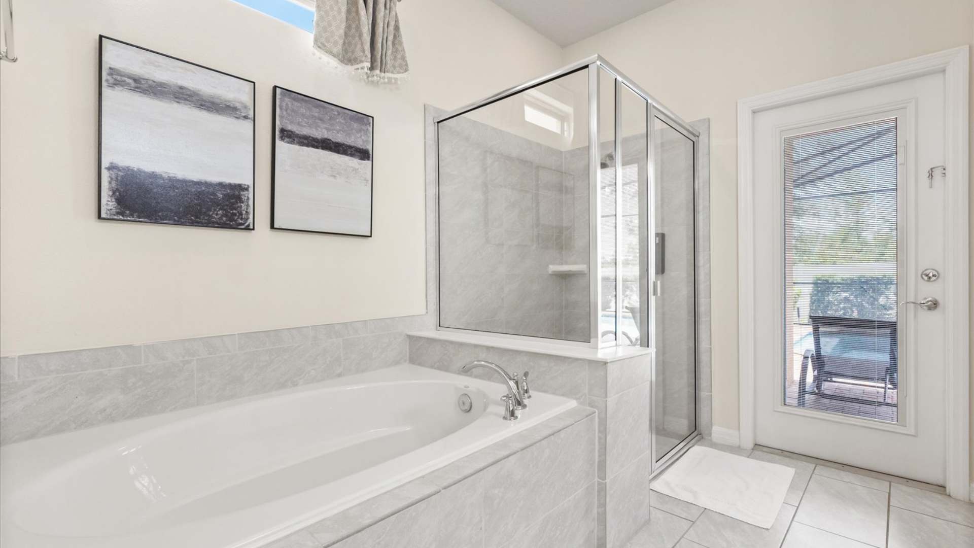 Bright bathroom showcasing a large white soaking tub and a glass-enclosed shower with light grey subway tiles, complemented by light-colored walls and a window above the tub for natural light.