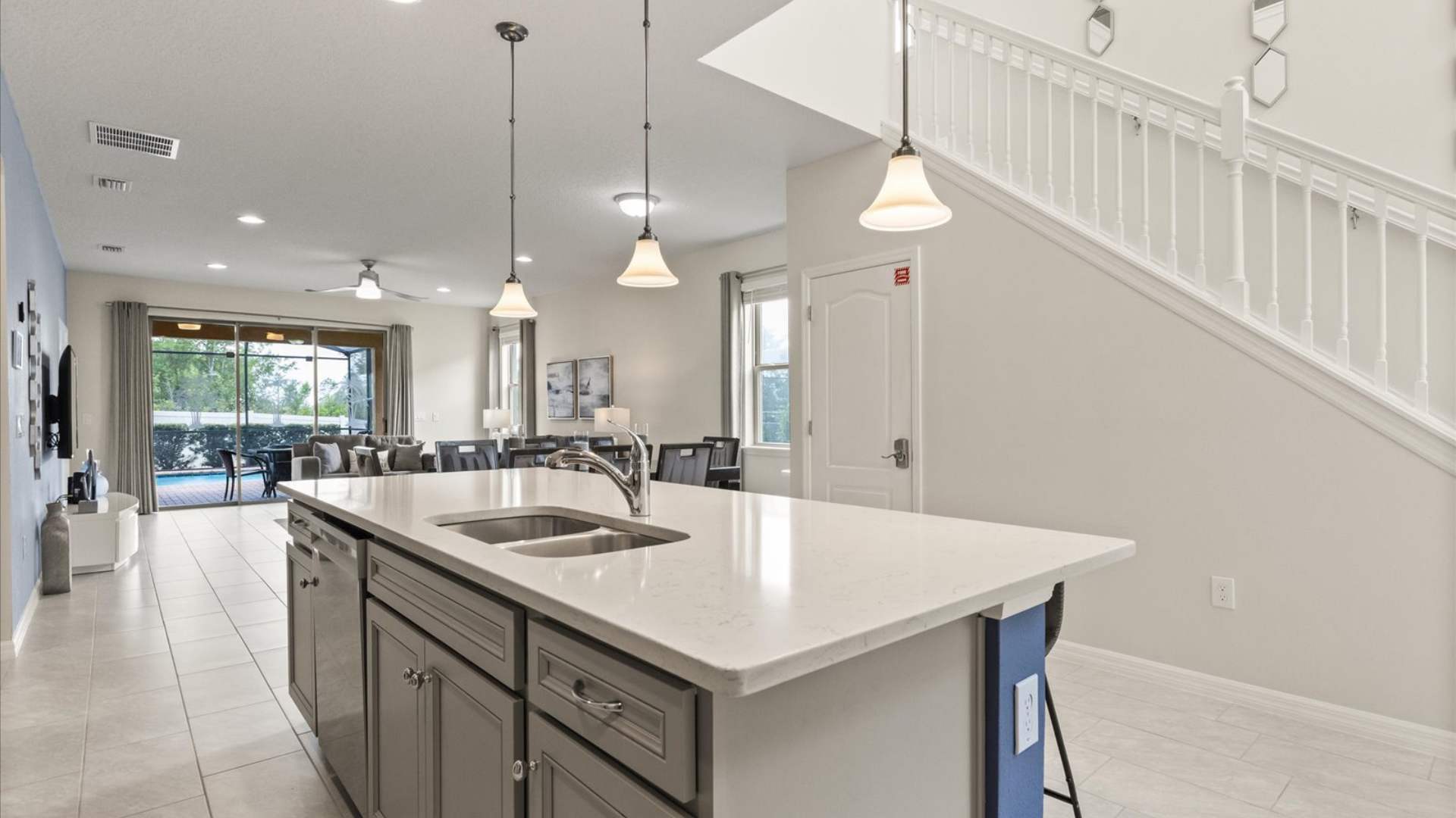 Kitchen island with a double sink and white quartz countertop, featuring pendant lights, and an open view towards the living area and the grand staircase.