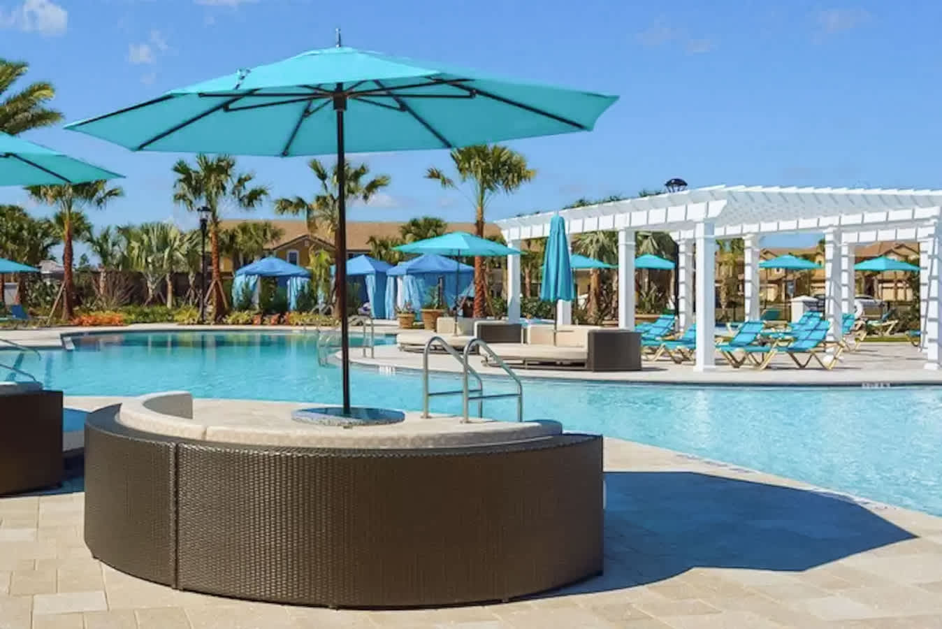 The main resort swimming pool with a circular in-water seating area, surrounded by lounge chairs, umbrellas, and a white pergola, offering a relaxing and spacious aquatic environment.