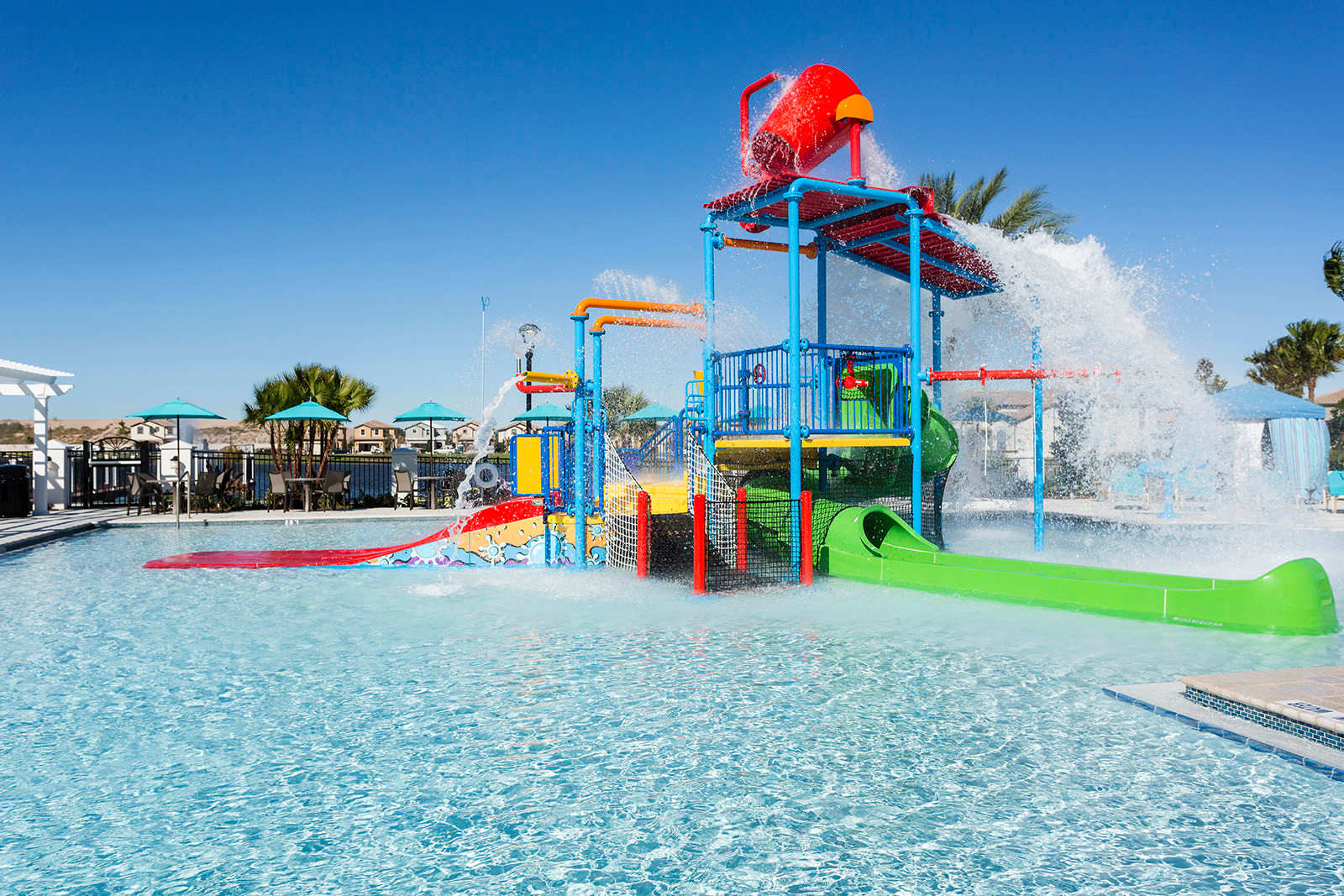A colorful and dynamic kids' water play area at the resort pool, featuring multiple slides, spray features, and a large dumping bucket, designed for family-friendly aquatic fun.