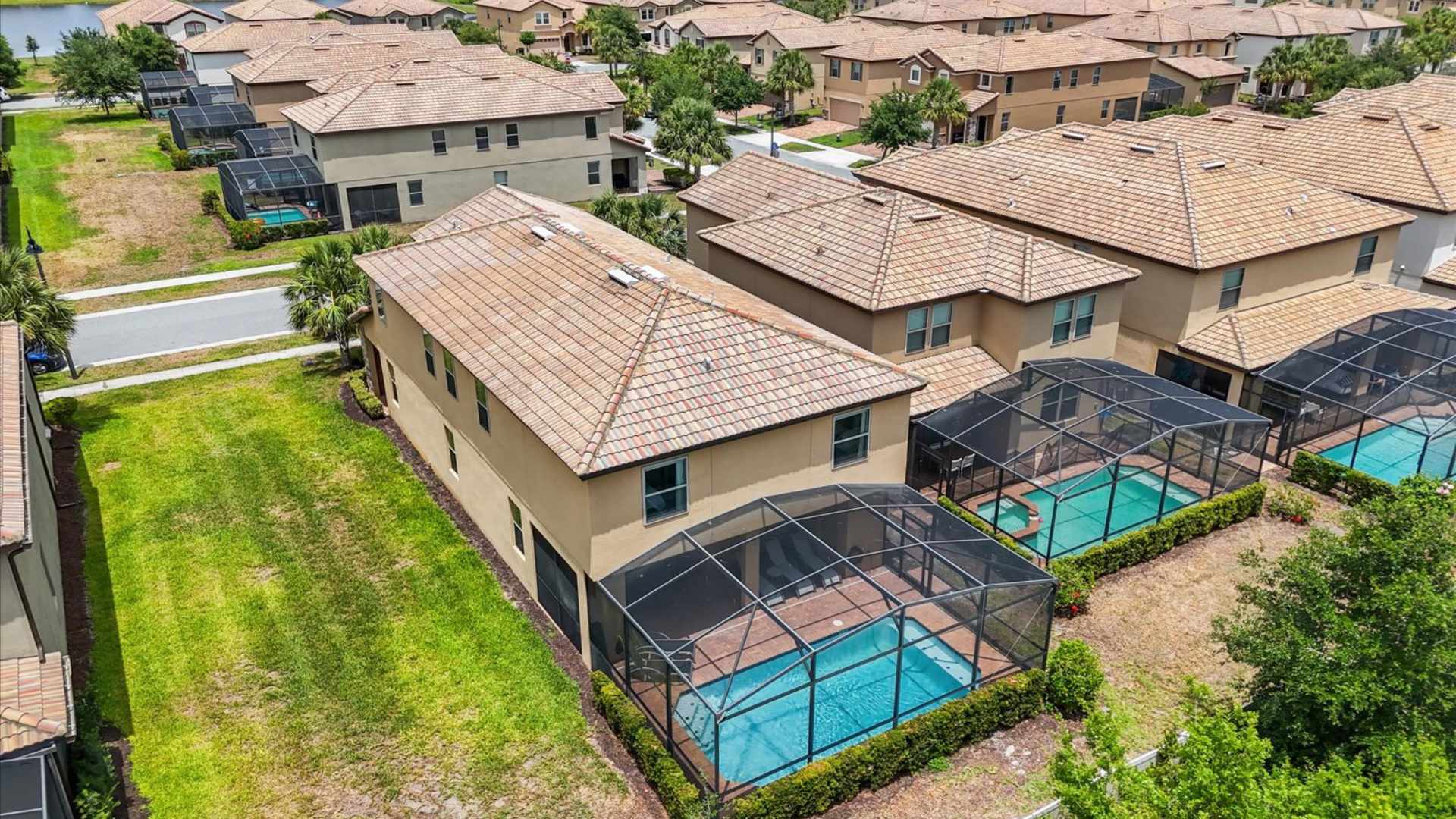 An aerial view of the two-story vacation home, highlighting its private screened-in pool area in the backyard, surrounded by green lawns and similar residential properties within a community.