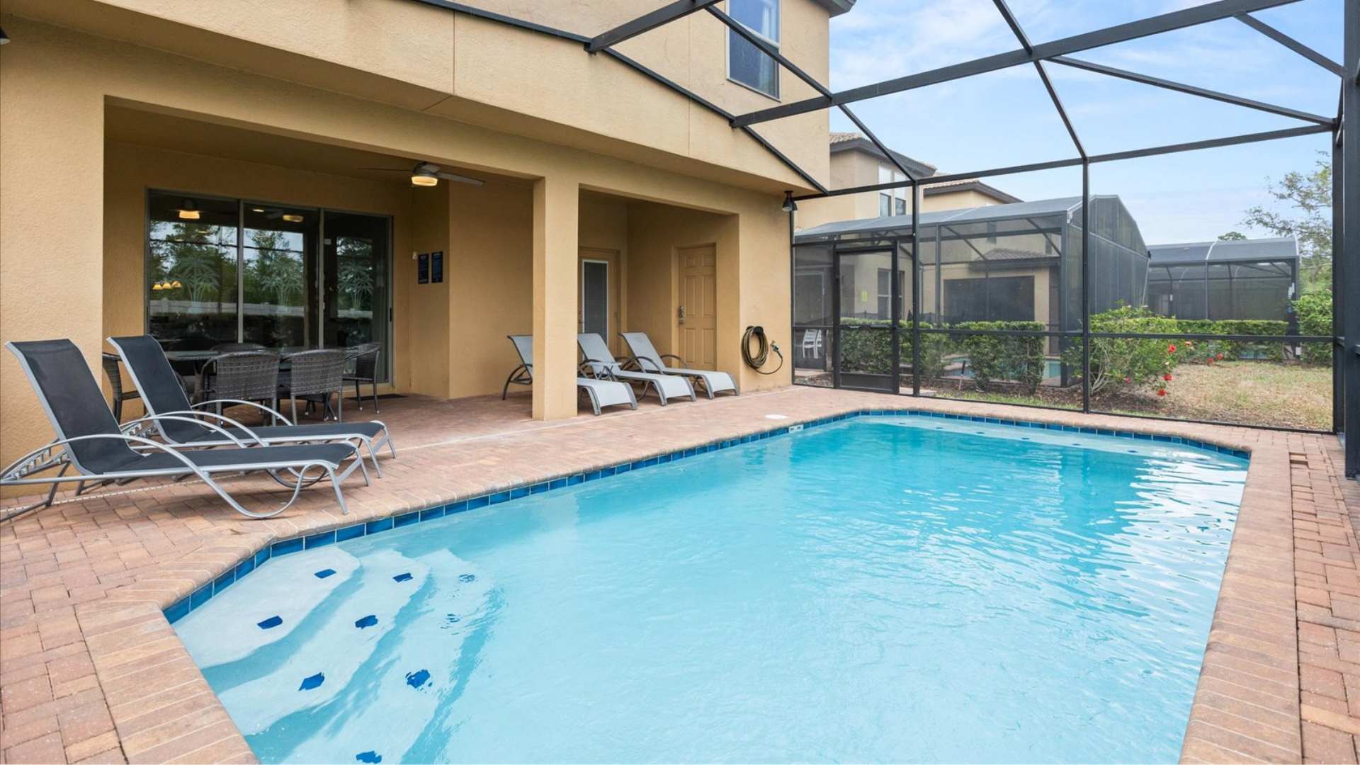 View of the private swimming pool and covered patio area from a different angle, showing lounge chairs by the pool and the house's exterior. The pool is enclosed by a screen cage.
