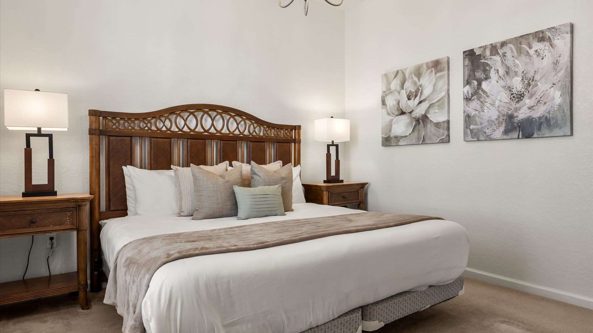 Close-up of the queen-sized bed in bedroom-2, featuring a distinctive woven wood headboard, neutral-toned bedding, and decorative pillows, flanked by wooden nightstands with contemporary lamps.