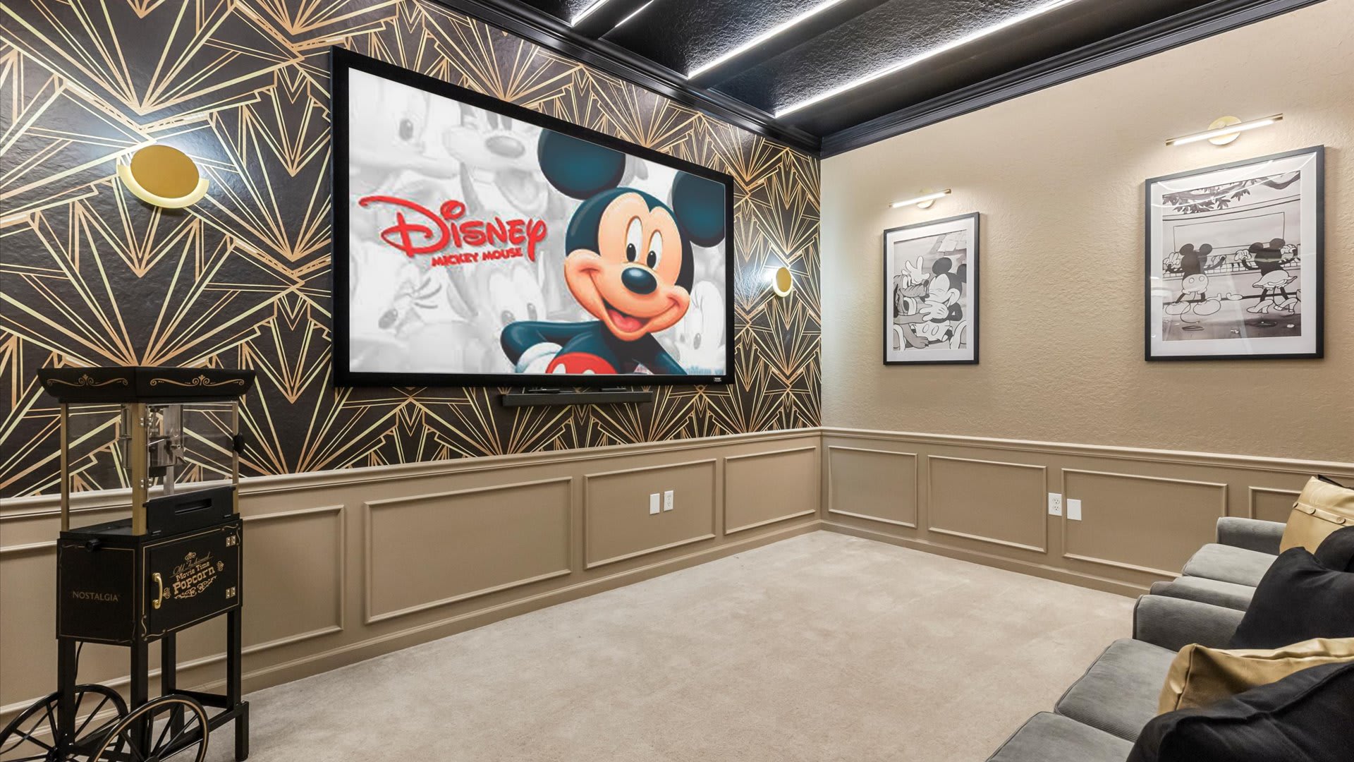A detailed view of the media room, highlighting the large screen displaying Disney content, the vintage popcorn machine, and the distinctive Art Deco wallpaper with gold accents.