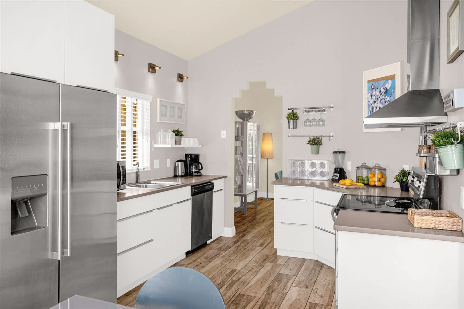 Wide view of the kitchen showcasing white cabinets, dark countertops, a large stainless steel refrigerator, and various appliances, with wood-look tile flooring and an arched opening to another room.