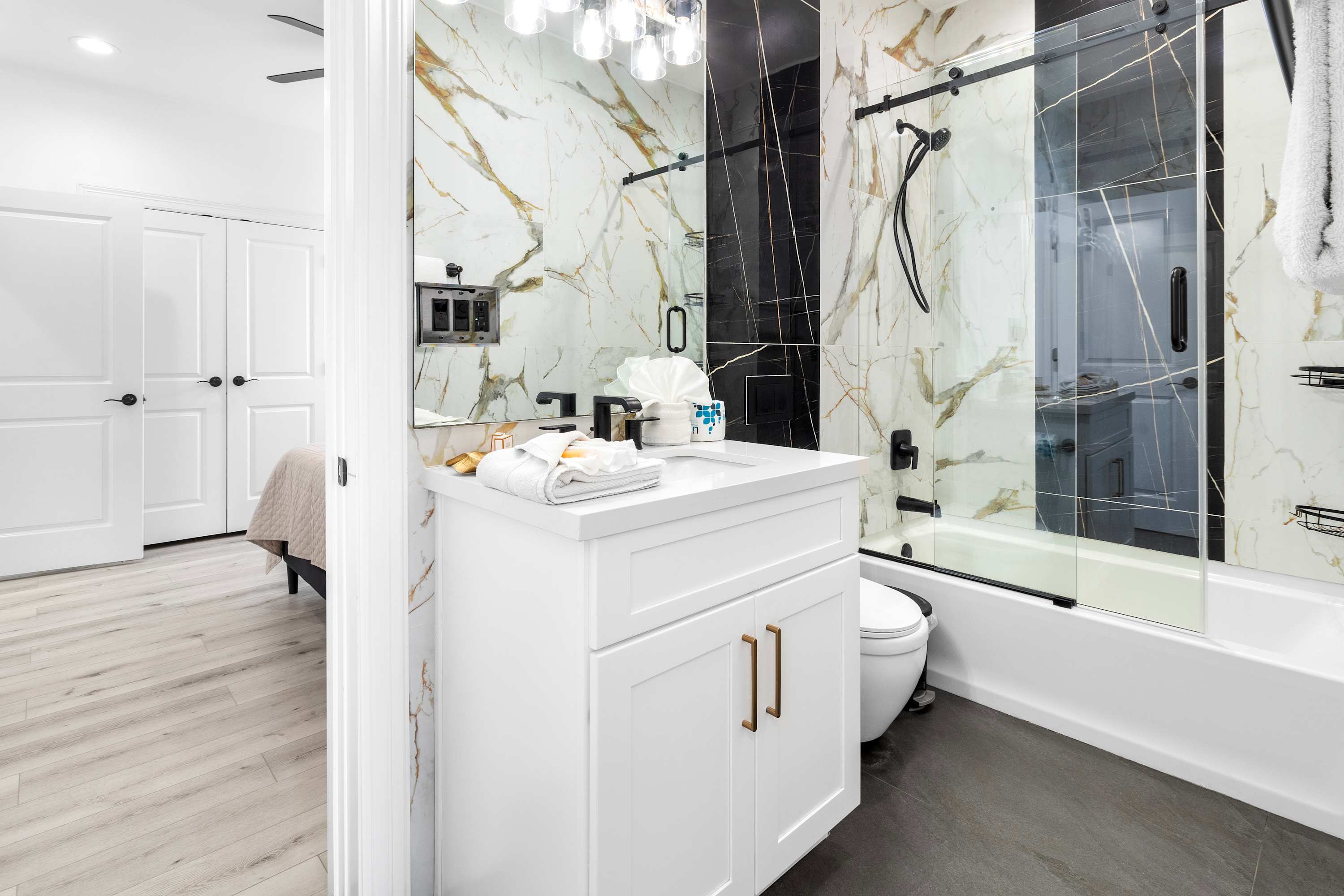 A luxurious bathroom featuring a white vanity with gold hardware, a large mirror, and a shower/tub combo with black and gold marble-patterned tiles and a black-framed glass enclosure.