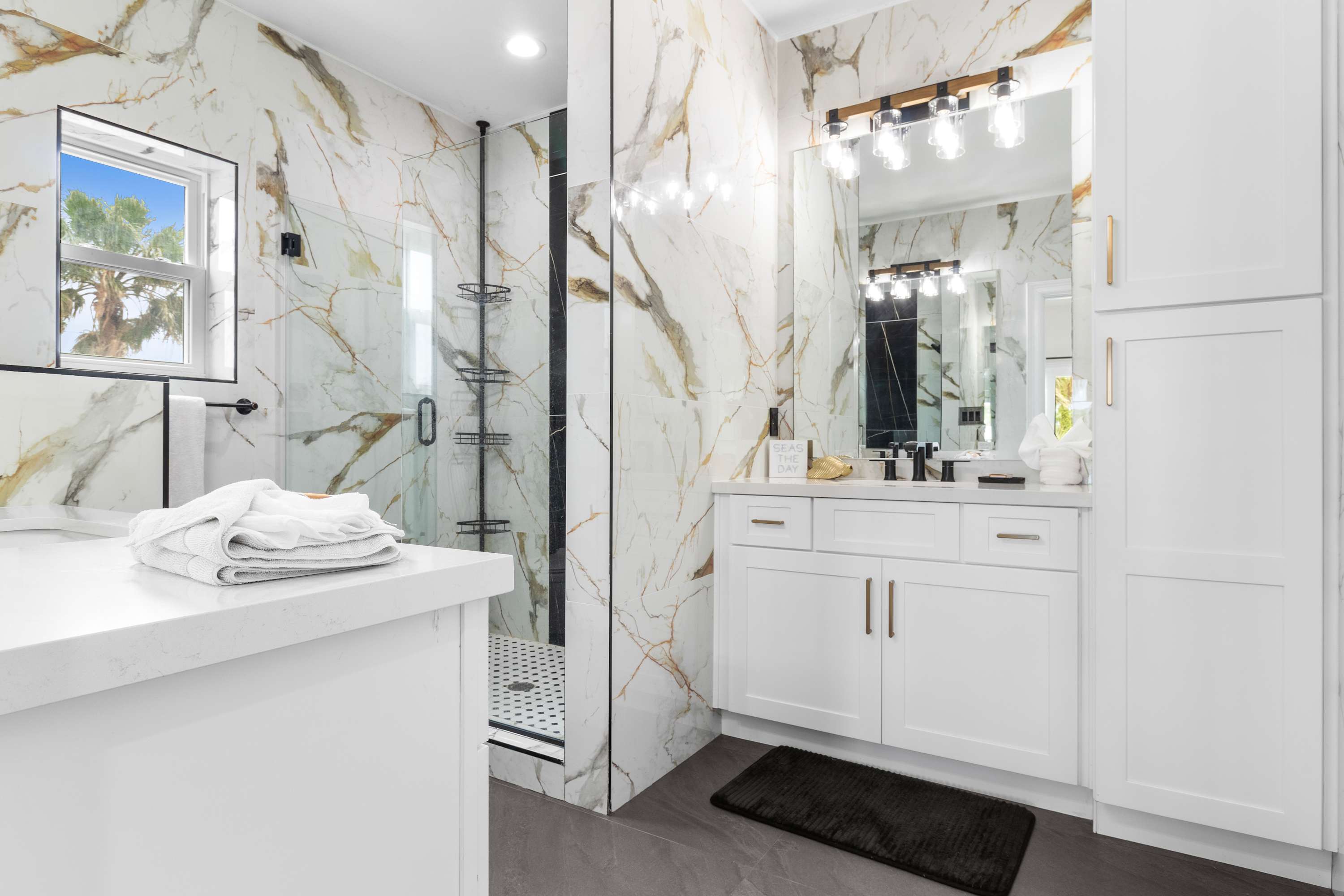 Luxurious bathroom with white and gold veined marble-look tile walls, a glass-enclosed shower with black and white mosaic floor, and a white vanity with a single sink and modern black fixtures.