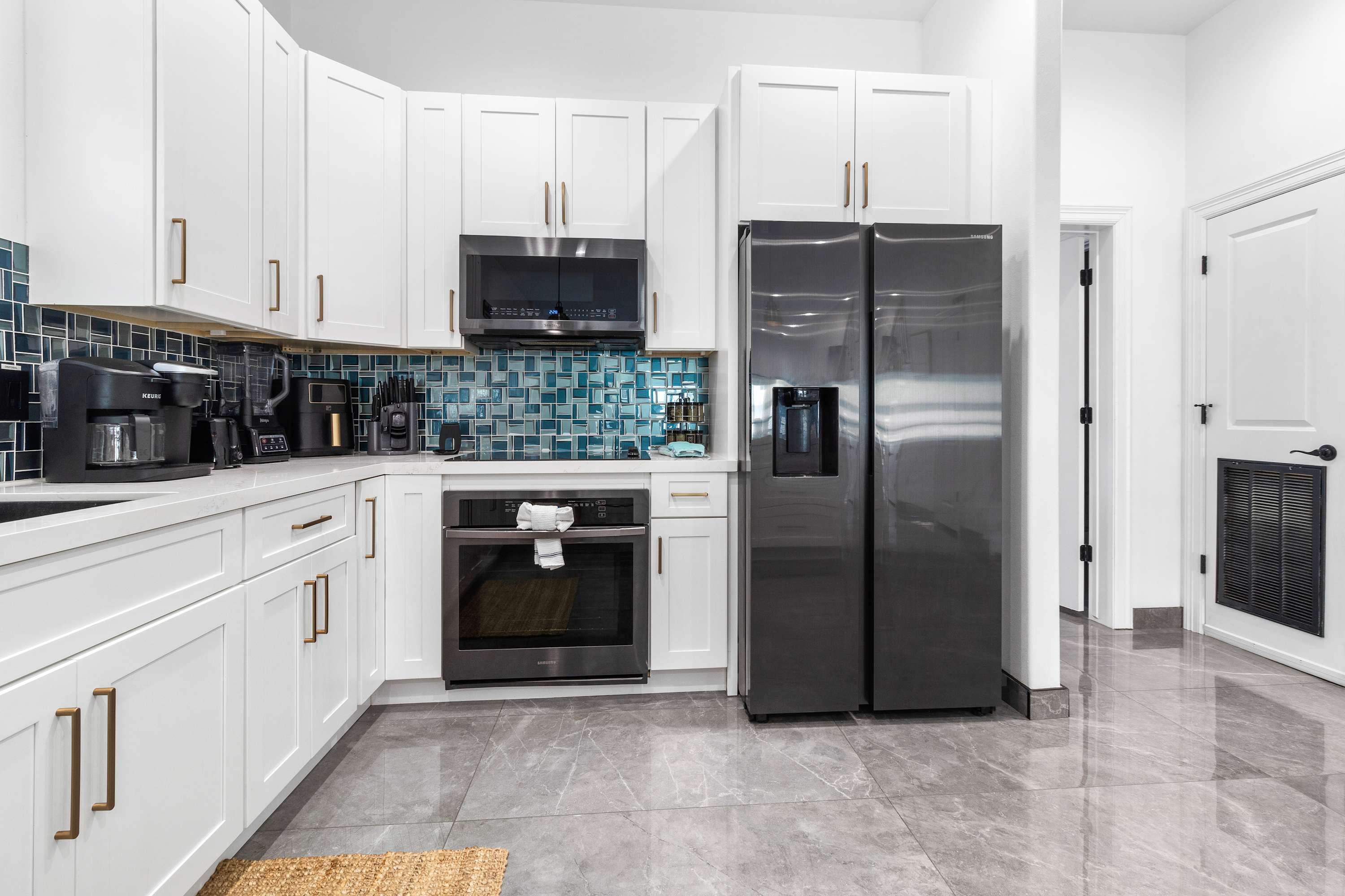 Detailed view of the modern kitchen showcasing white shaker cabinets, a built-in microwave, and a dark grey oven. The blue mosaic tile backsplash provides a vibrant contrast to the clean white surfaces.