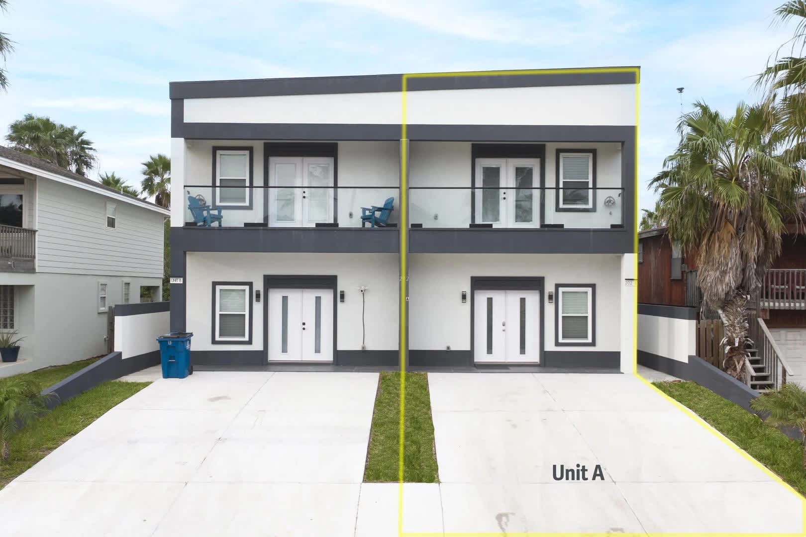 The modern front exterior of a two-story townhouse duplex, featuring a striking dark gray and white facade with multiple balconies and large glass doors. Two concrete driveways lead to separate entrances, with "Unit A" highlighted on the right side.