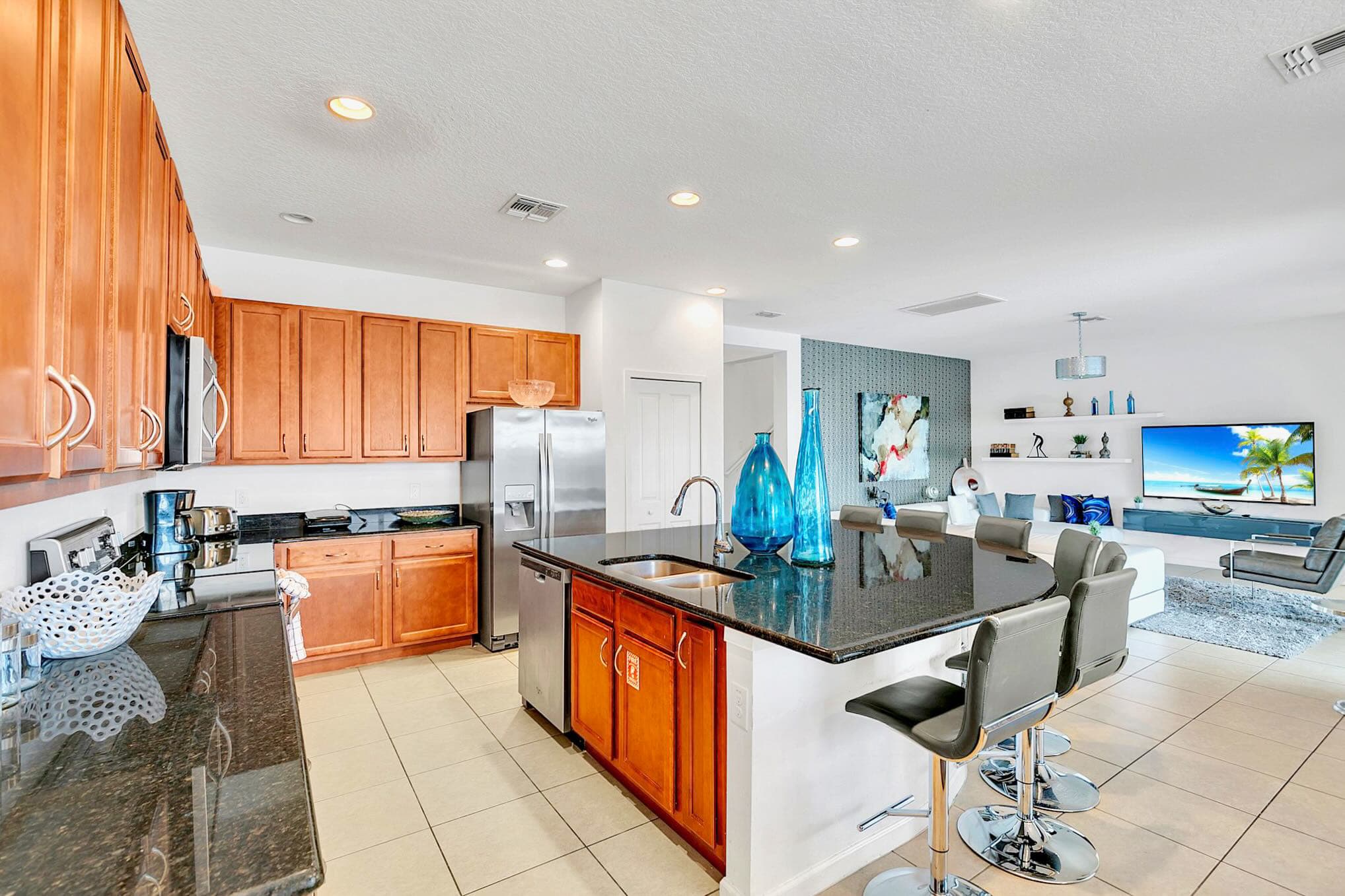 Expansive open-concept view from the kitchen, highlighting the large island and connecting to the living room with its white sectional sofa and accent wall, all on light tile flooring.