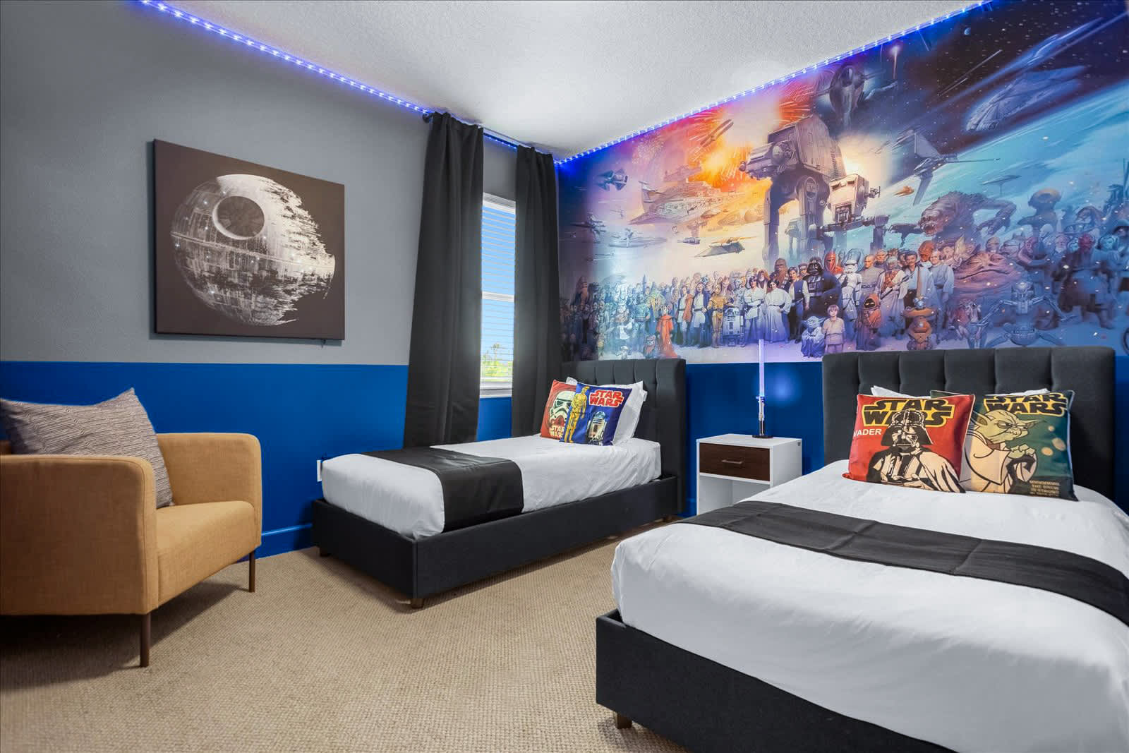 Star Wars-themed bedroom featuring a large wall mural and a Death Star canvas art piece. Two twin beds with themed pillows are arranged, and a mustard yellow armchair adds a pop of color.