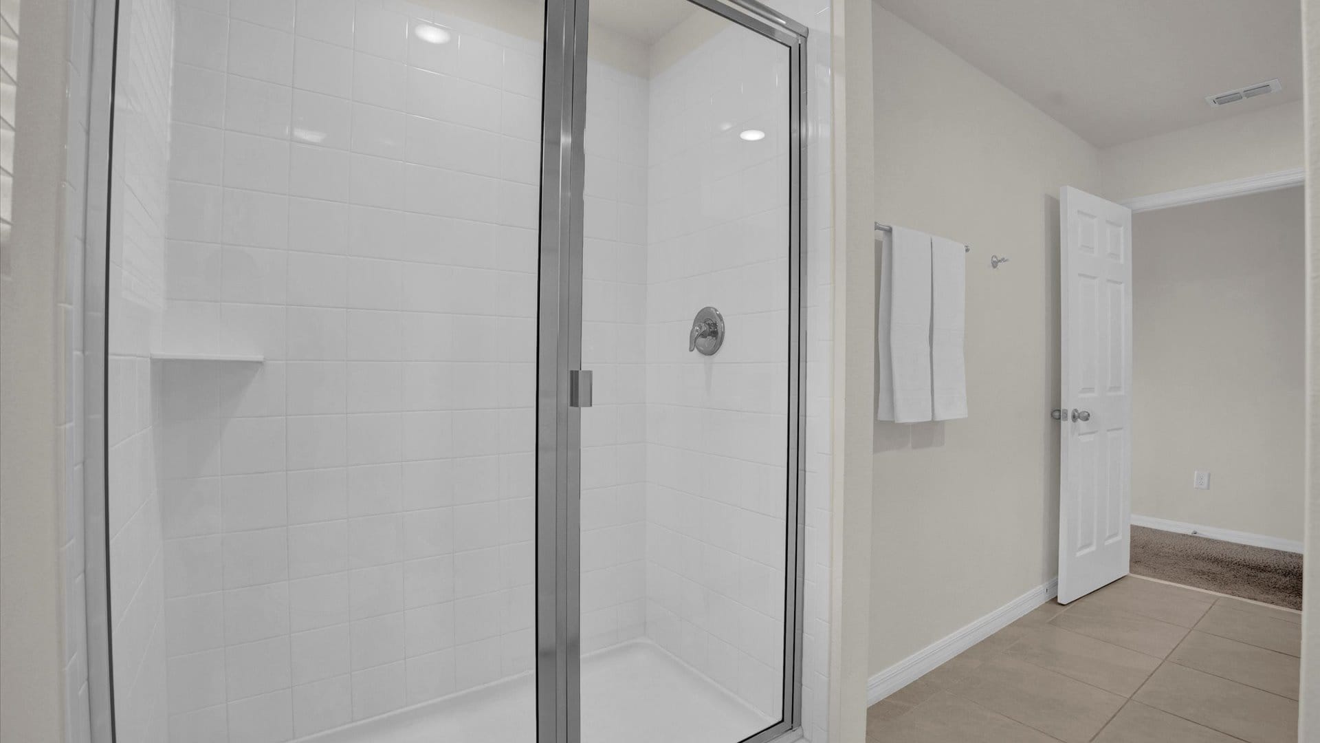 A modern walk-in shower with white subway tiles and a clear glass enclosure. A built-in shelf is visible, and the shower head is chrome.