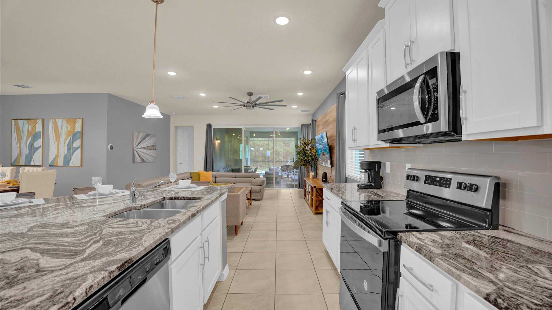 Contemporary kitchen with white shaker cabinets, granite countertops, and stainless steel appliances including a stove and microwave. The open layout provides a clear view into the living room, fostering a connected living experience.