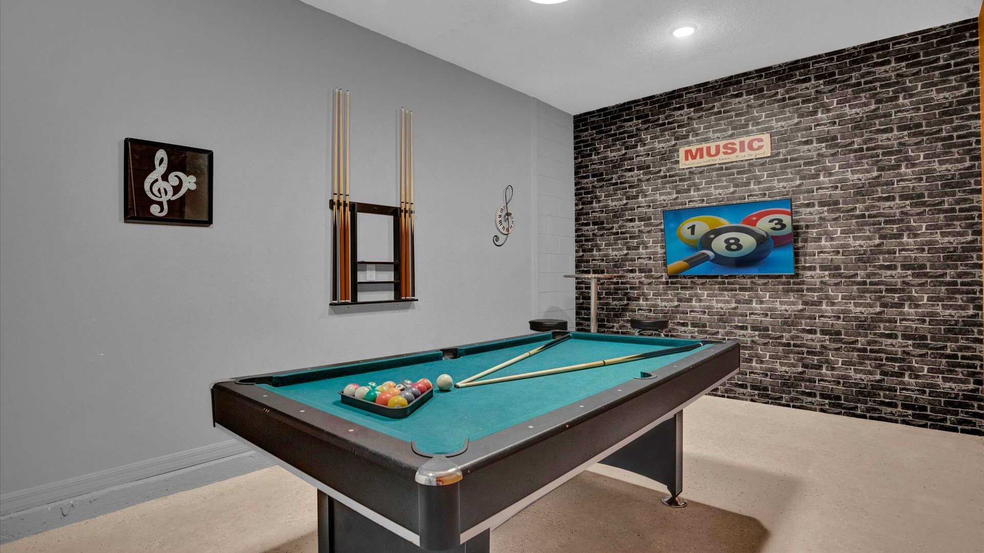 A vibrant game room centered around a green-felt pool table, with a large TV mounted on a dark brick accent wall displaying a billiards image. Music-themed wall art and cue racks complete the entertainment space.