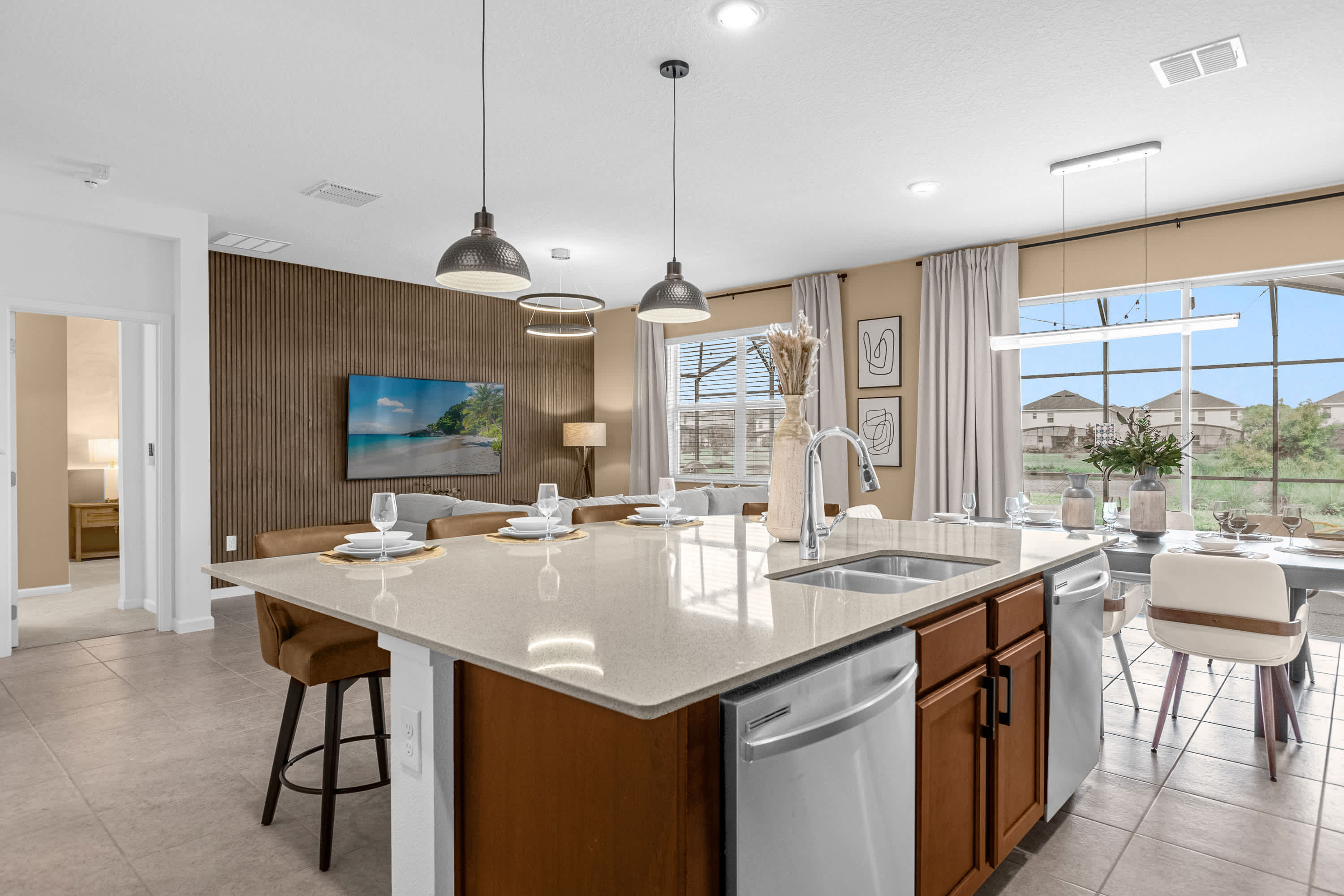 Modern kitchen featuring a large island with a sink and bar seating, light quartz countertops, and stainless steel appliances. The open layout connects to the dining and living areas, visible in the background.