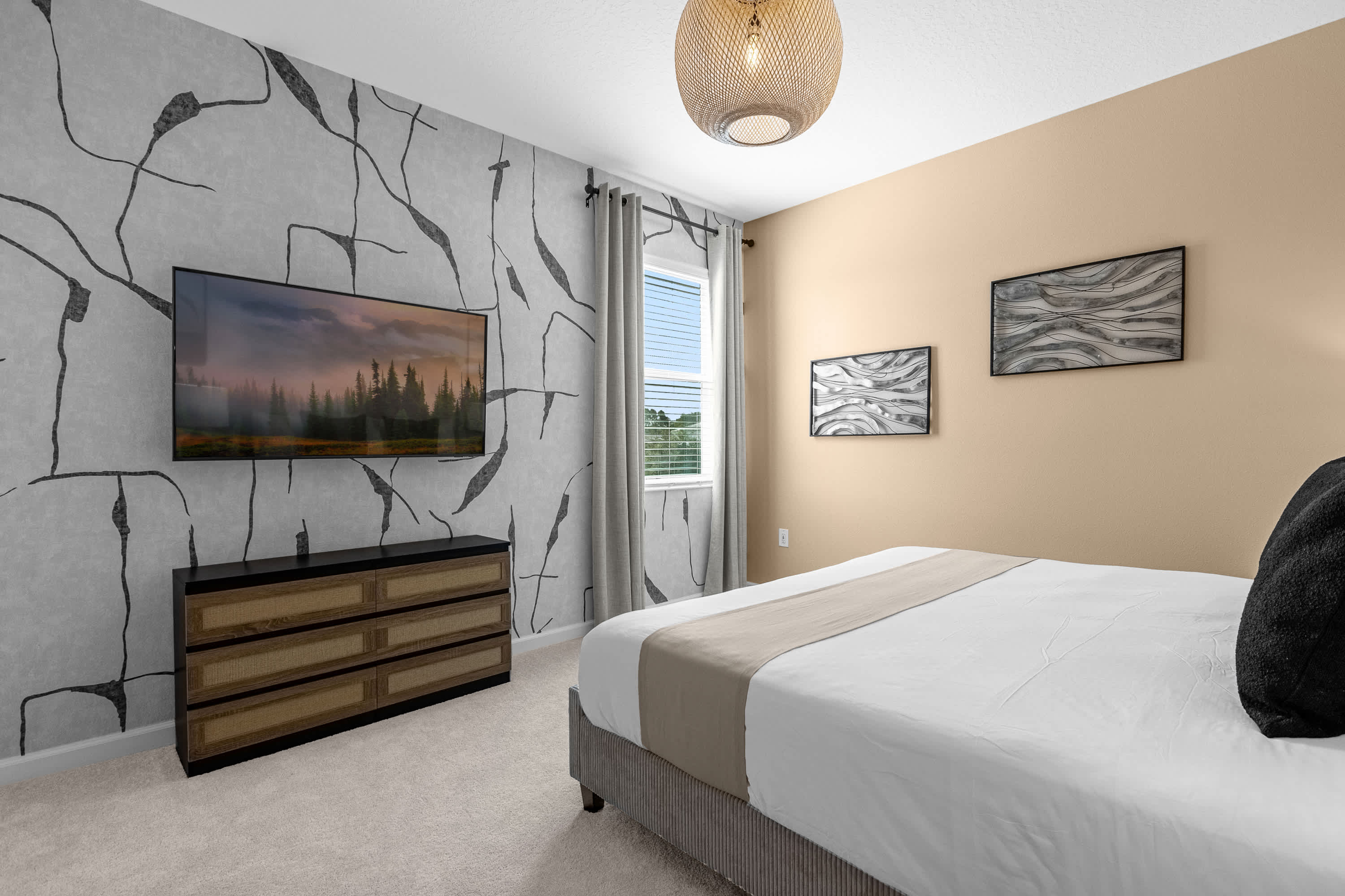 Modern bedroom with a king bed, light beige walls, and a striking grey and black abstract wallpaper accent wall with a wall-mounted TV. A woven pendant light hangs from the ceiling.