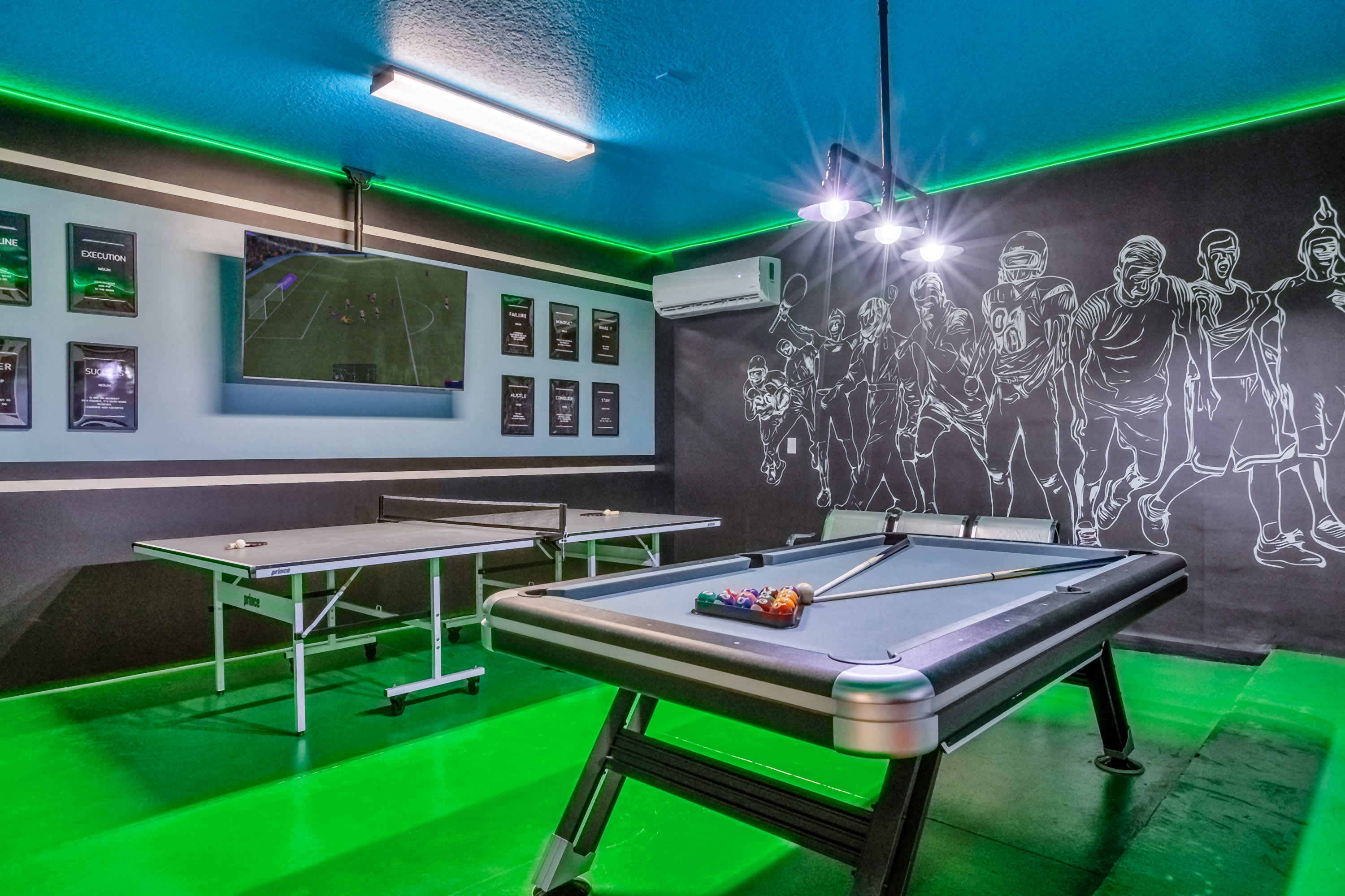 Vibrant game room with a bright green floor and ceiling, featuring a pool table with colorful balls and a ping-pong table. A large mural of athletes is on the black accent wall, and a TV is mounted above the ping-pong table.