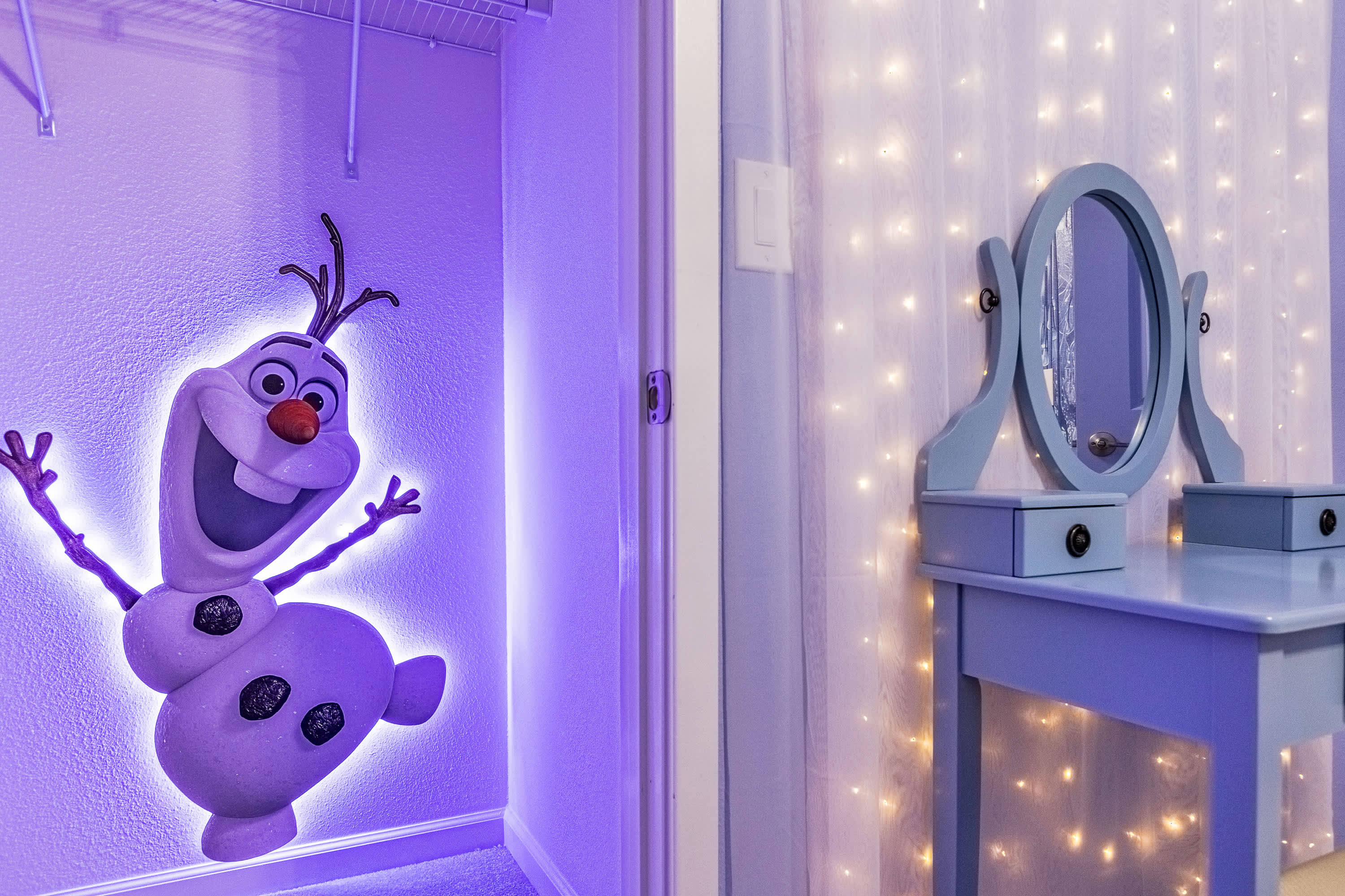 A close-up view within a themed children's bedroom, showcasing a light-up Olaf character cutout on the wall next to a closet. A light blue vanity table with a mirror and string lights on the wall are also visible, contributing to the enchanting atmosphere.