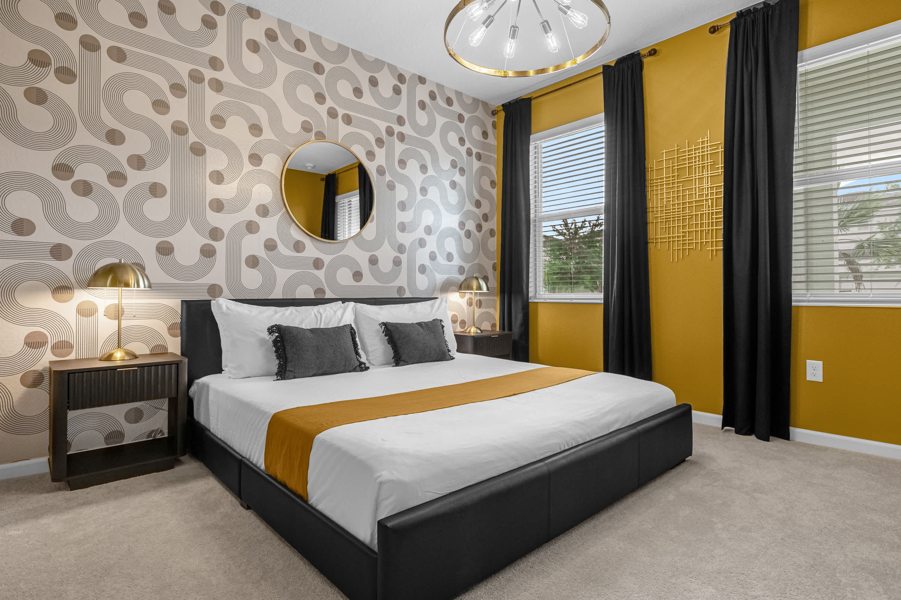 A modern bedroom featuring a black platform bed with white and gold bedding, flanked by dark wood nightstands with gold lamps. The room boasts a striking patterned wallpaper on one wall and a solid gold accent wall with black curtains, creating a bold aesthetic.