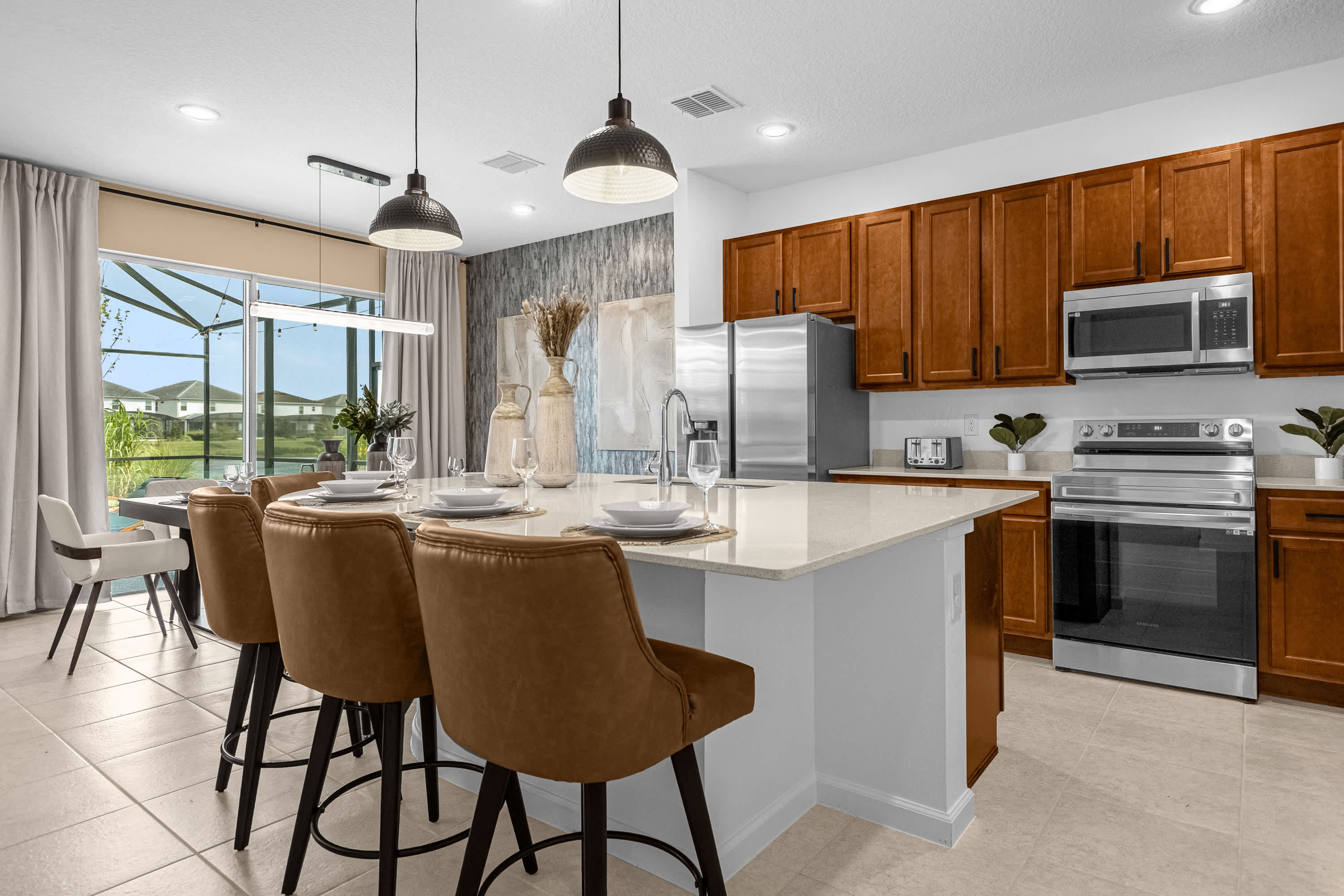 Bright kitchen with a large island offering bar seating, light countertops, and wooden cabinets. It seamlessly connects to the dining area with a dark table and white chairs, and features modern pendant lighting.