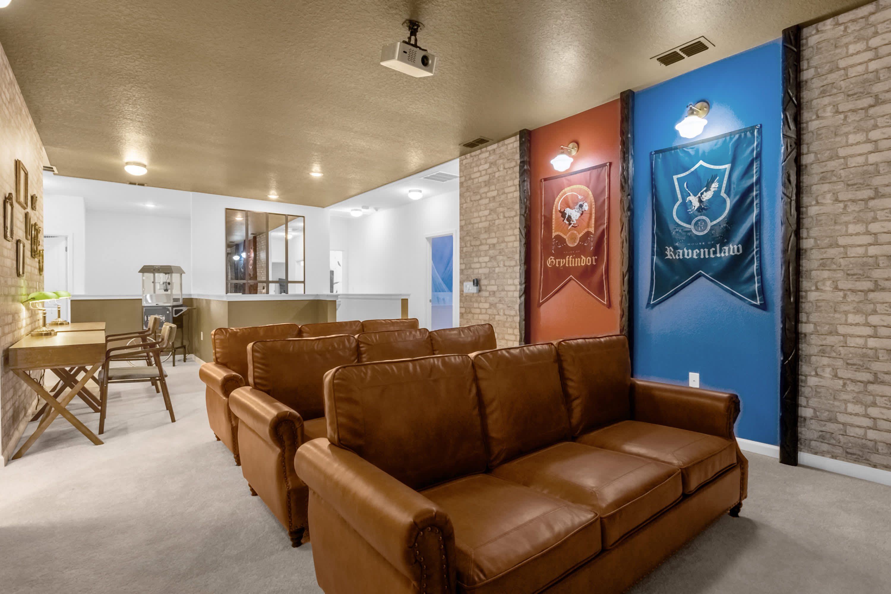 Another view of the Harry Potter-themed media room, showing the back of the seating area and a small desk space to the left. The faux brick walls and house banners are prominent, with a popcorn machine visible in the background.