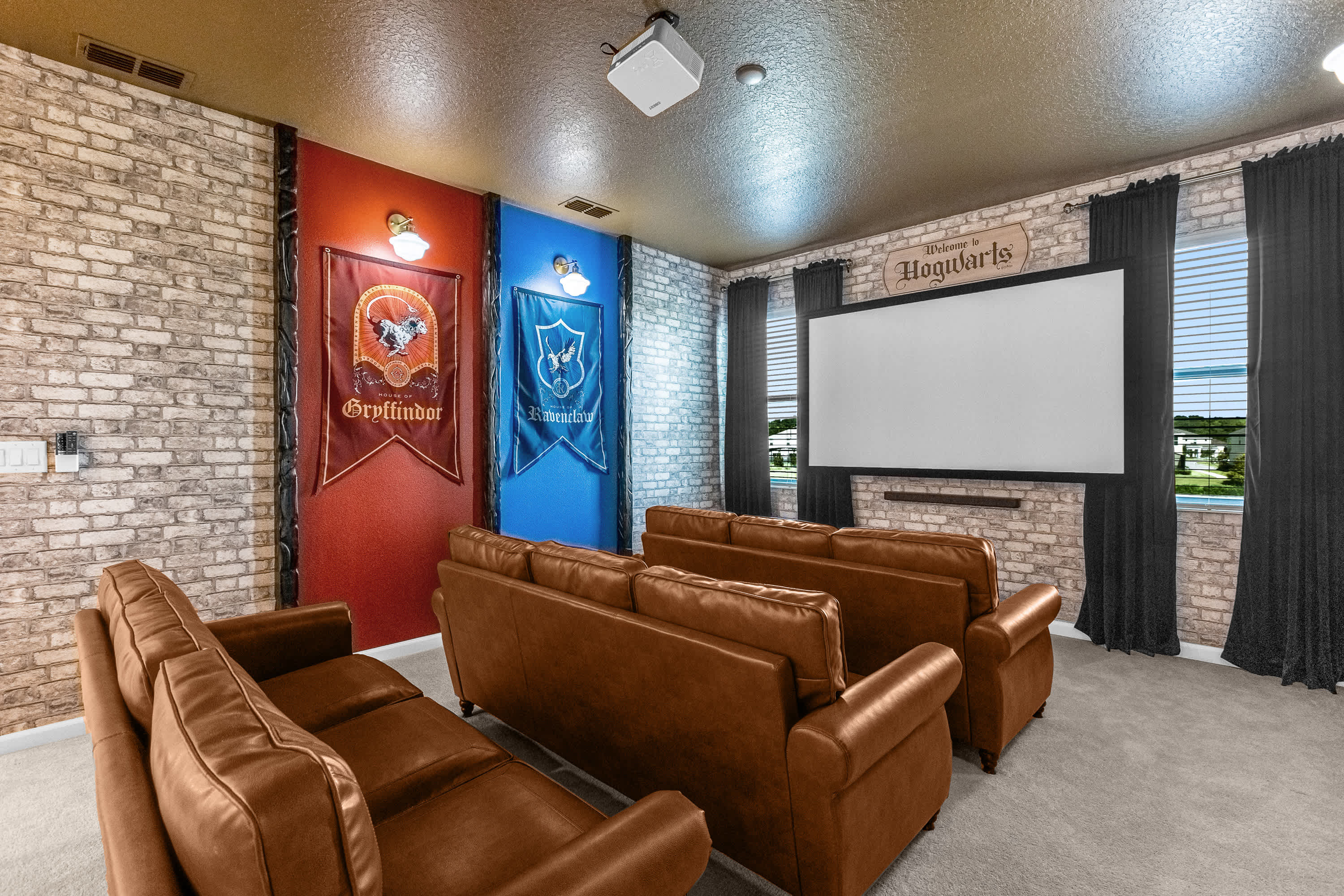 Harry Potter-themed media room featuring two rows of brown leather sofas facing a large projection screen. The walls are decorated with faux brick and large Gryffindor and Ravenclaw banners.
