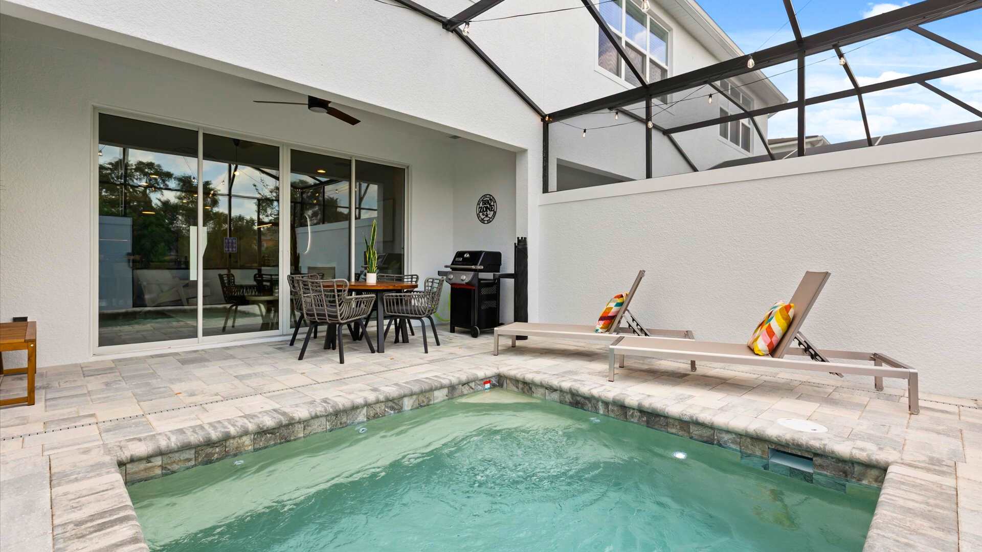 Spacious screened-in patio with a private plunge pool, two modern lounge chairs, and an outdoor dining set. The area is paved with light-colored stones and includes a BBQ grill, offering a relaxing outdoor living space.