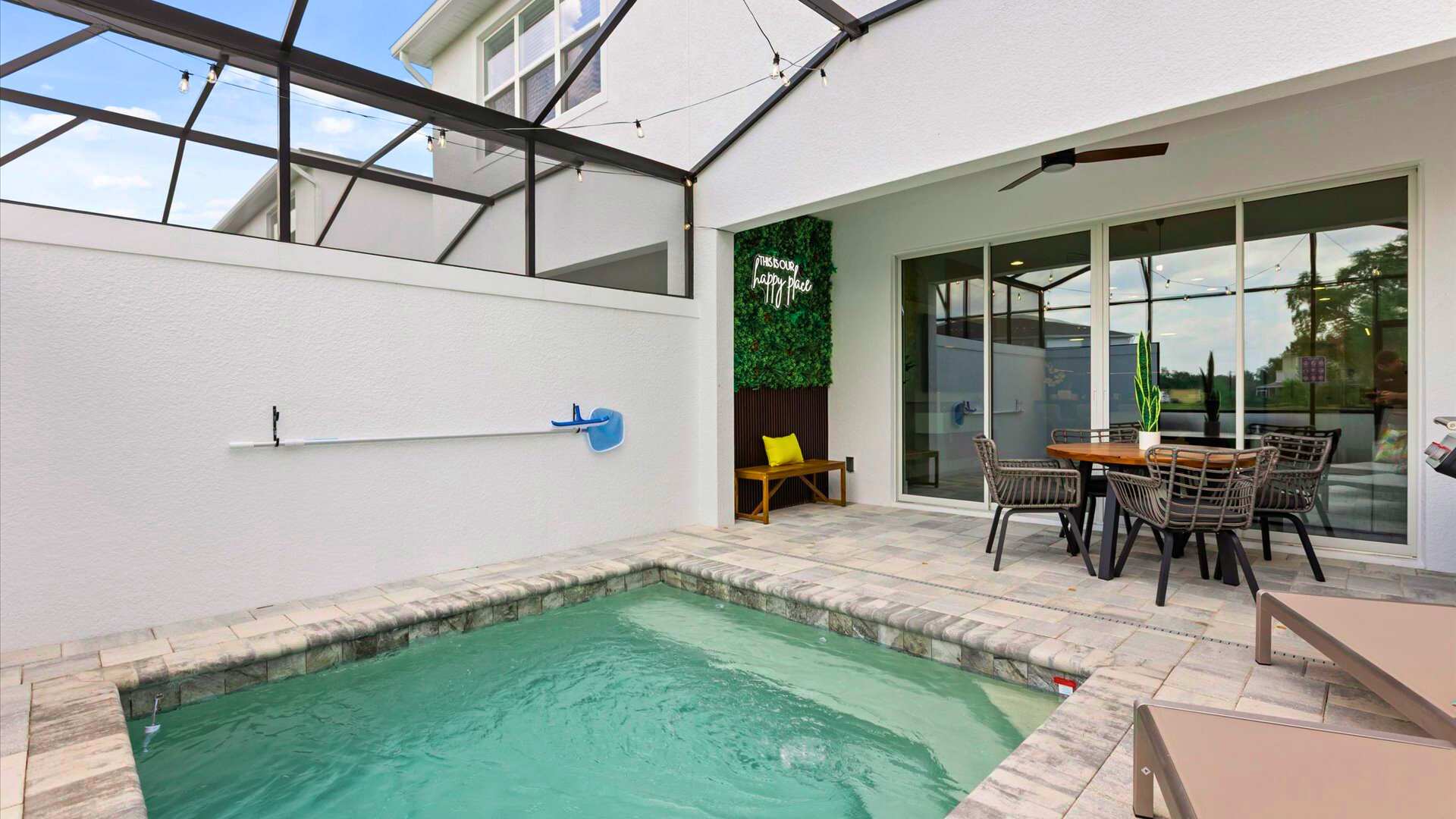 An enclosed outdoor patio features a small private pool with tiled coping, a dining area with a round table and chairs, and a green wall with a 'Happy Place' neon sign.
