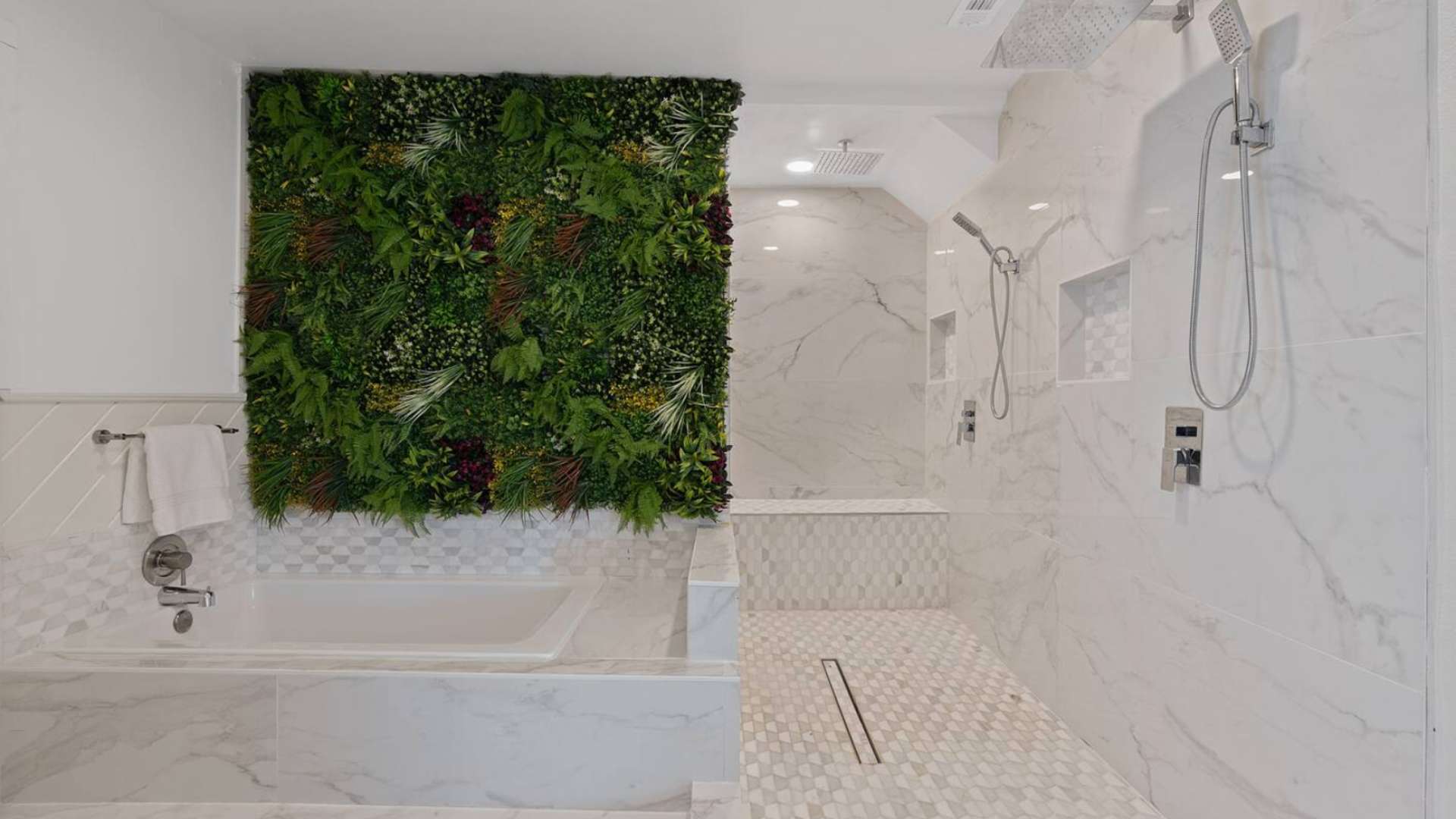A luxurious bathroom featuring a deep soaking tub with a vibrant green living wall above it, and a spacious walk-in shower with white marble tiles and dual shower heads.