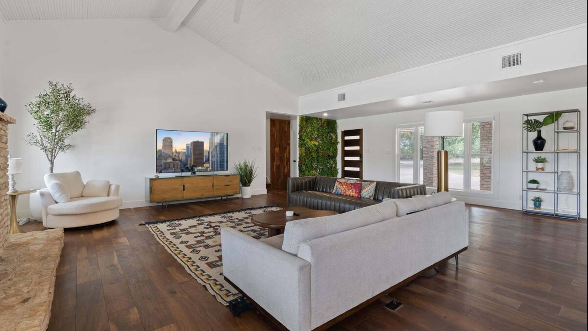 Bright living room with vaulted white ceiling, dark hardwood floors, a large sectional sofa, and a striking green living wall feature, centered around a modern media console with a TV.