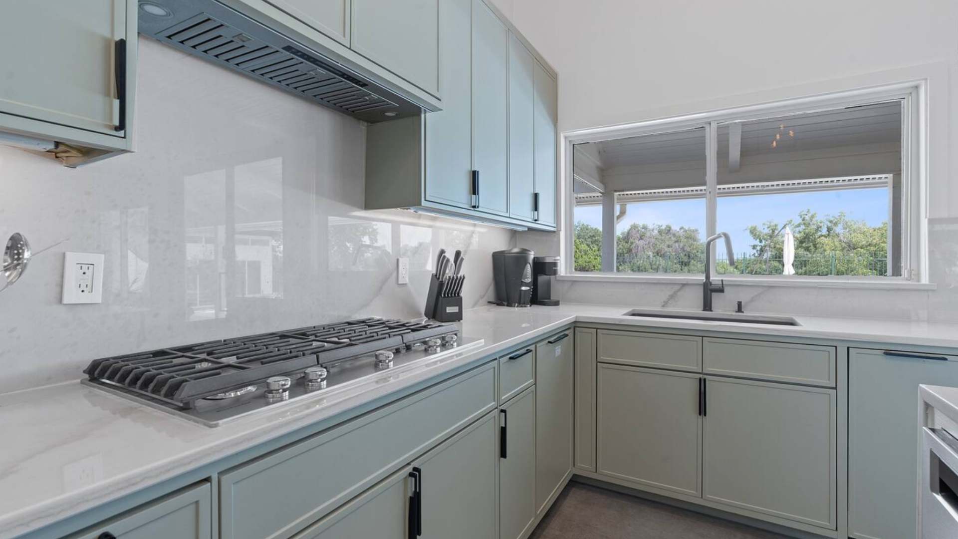 Detailed view of the kitchen counter with a sleek gas cooktop, white marble-look backsplash, and a black faucet over the sink, with a large window offering an outdoor view.