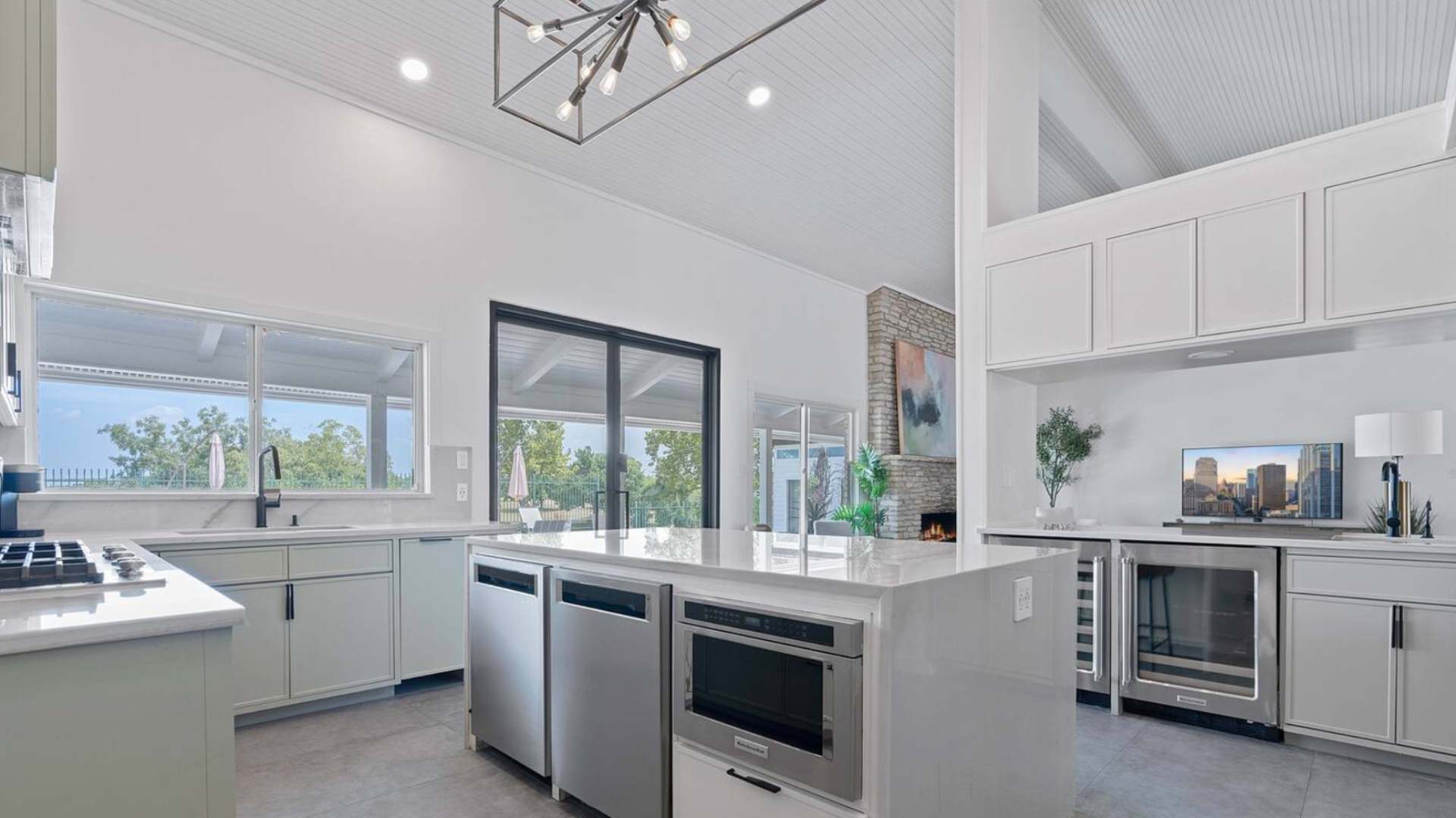 Bright kitchen with a large white quartz island featuring built-in appliances, light green cabinetry, and a view into the living room and out to the pool area through sliding glass doors.
