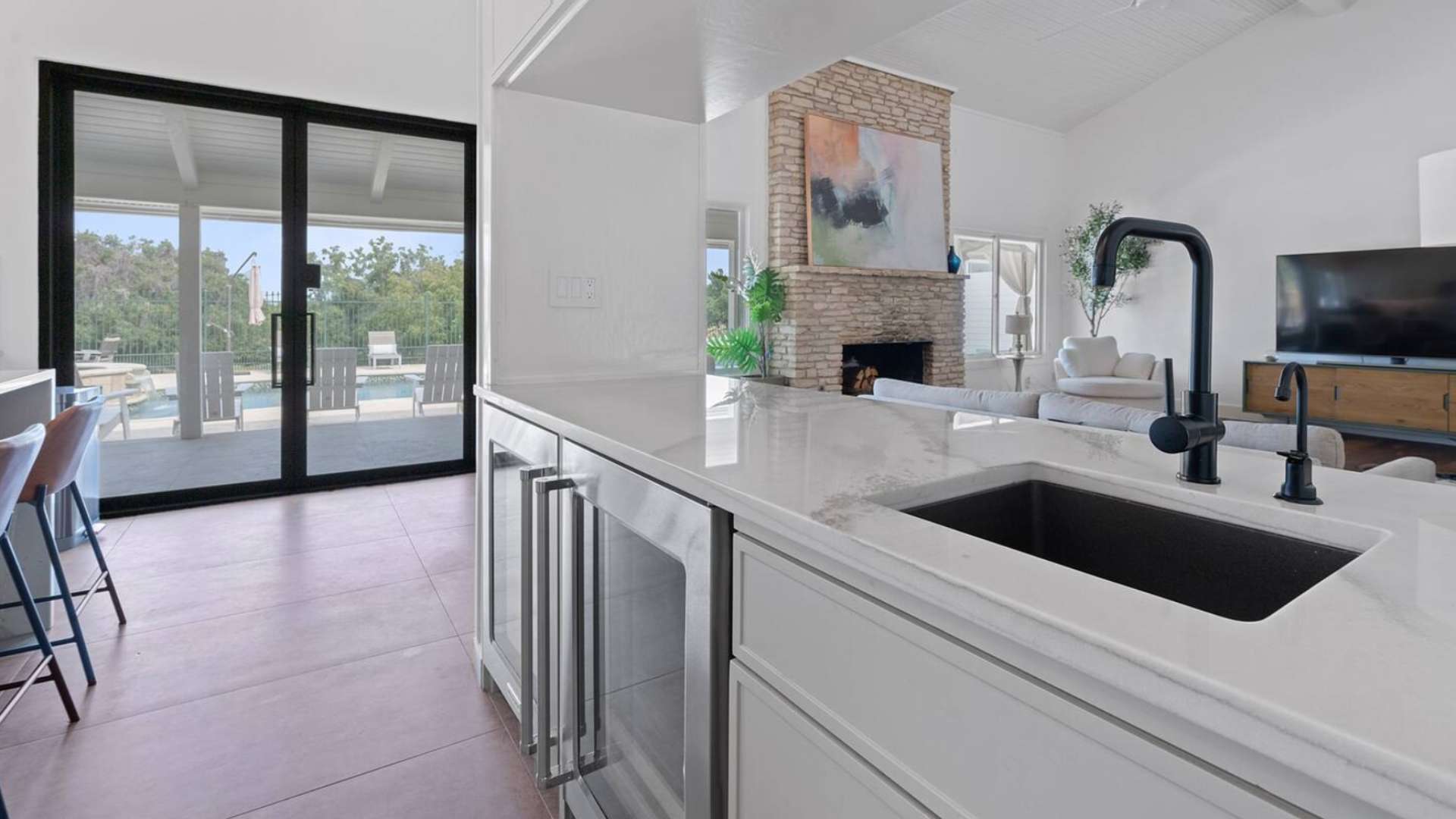 Kitchen island with an undermount sink and black faucet, showcasing built-in beverage coolers, and offering a direct view of the outdoor pool and patio through large sliding glass doors.