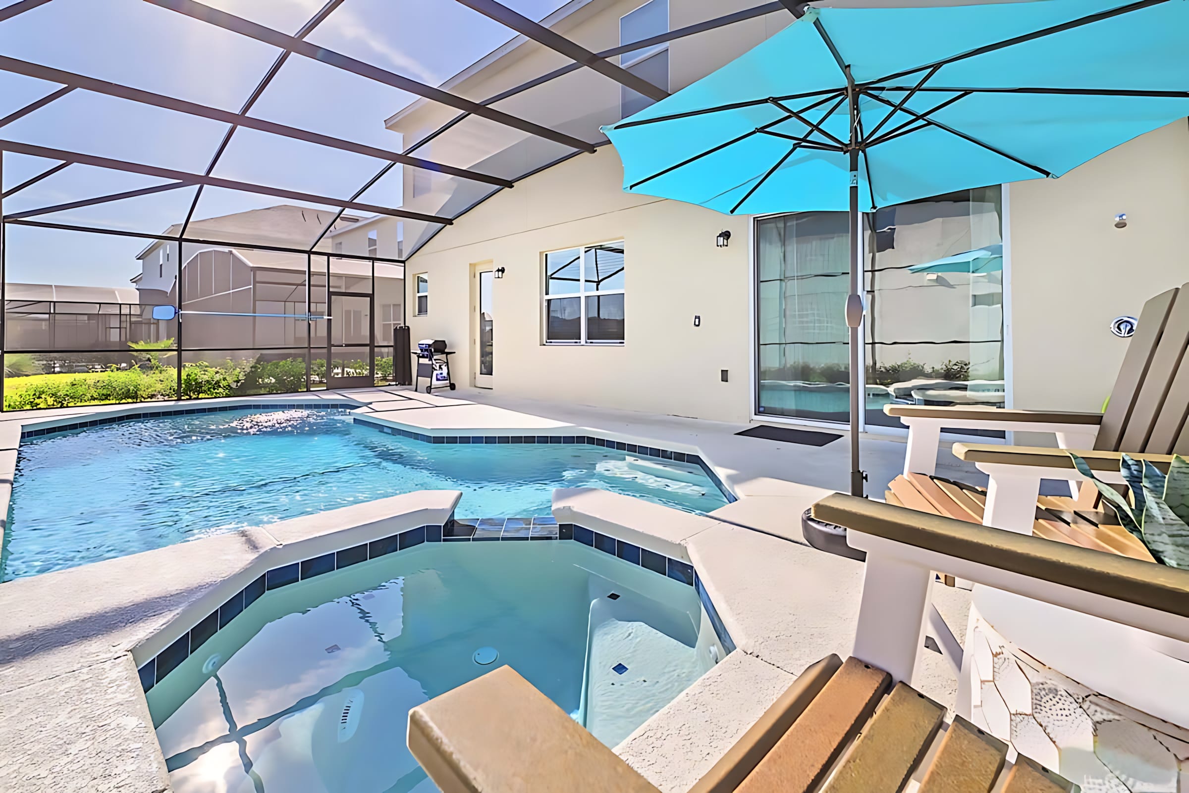 Screened-in private pool area with a rectangular pool and an attached hot tub, featuring a bright turquoise umbrella and two wooden Adirondack chairs on the surrounding patio. A BBQ grill is visible near the house wall.