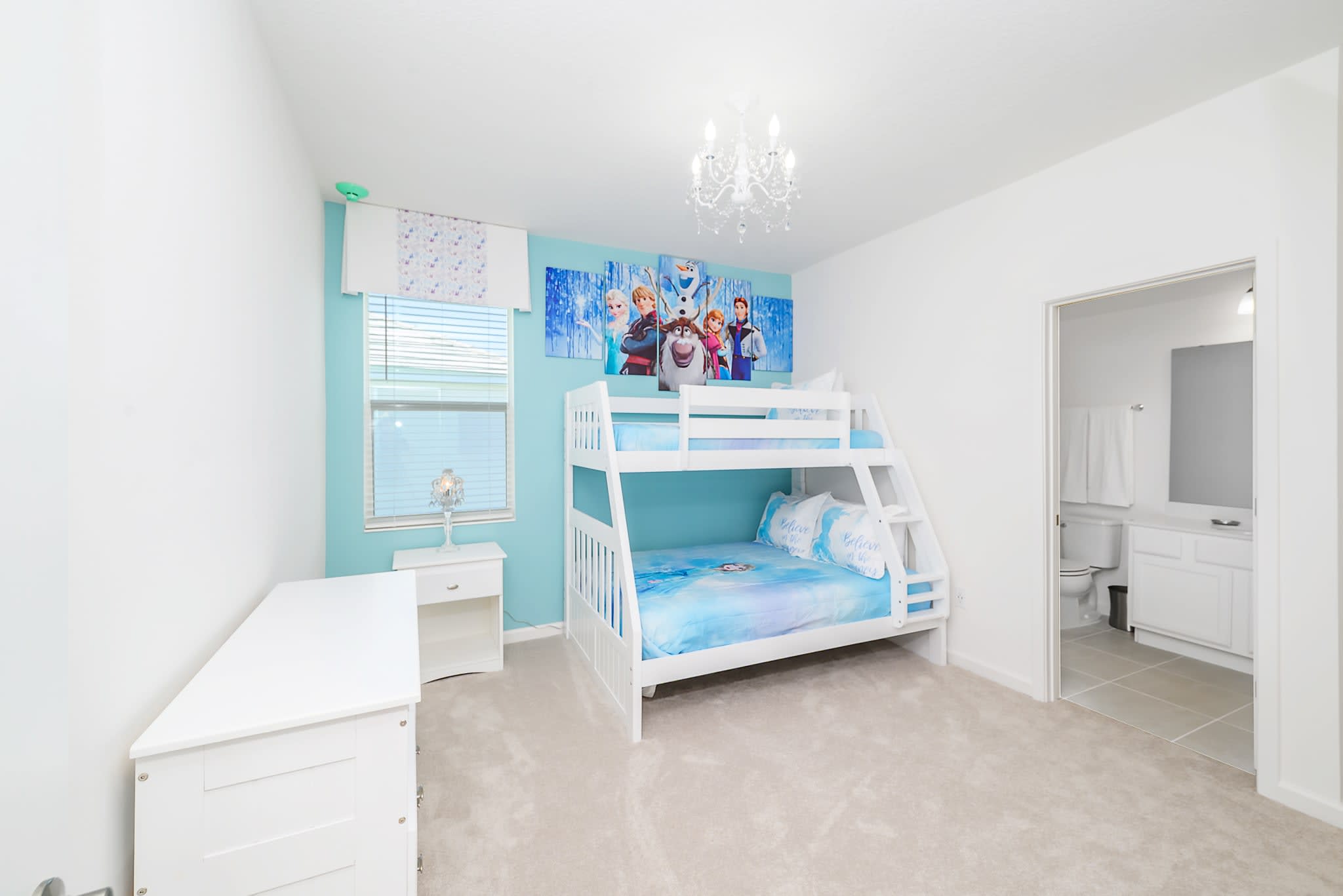 A Frozen-themed bedroom featuring a white bunk bed, a light blue accent wall, and large wall art depicting characters from Frozen. The room is furnished with a white dresser, a nightstand, and a decorative chandelier.