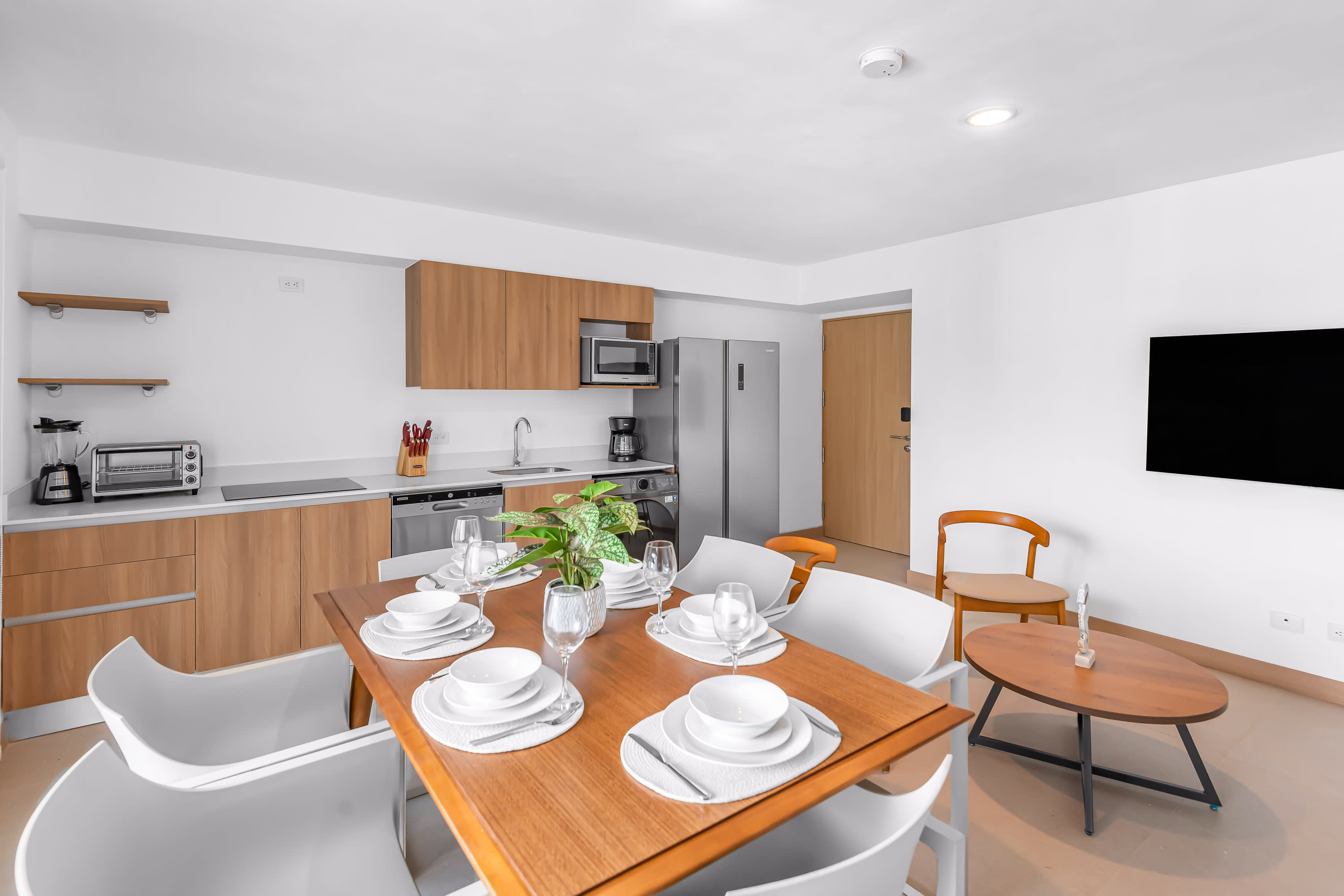 Contemporary kitchen with light wood flat-panel cabinetry, white countertops, and stainless steel appliances including a refrigerator, microwave, dishwasher, and a combined washer/dryer unit.