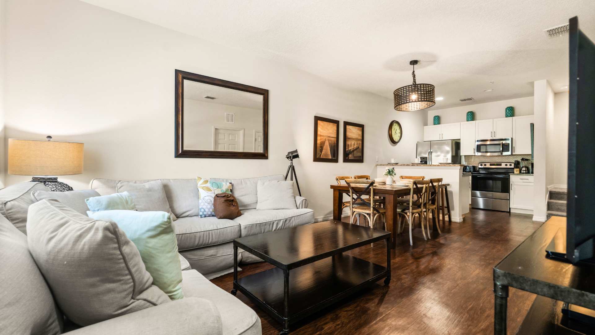 A wide view of the open-concept living area showcases dark hardwood floors, a light gray sectional sofa, and a black coffee table. The dining area and a glimpse of the kitchen are visible in the background, creating a cohesive and inviting main floor.