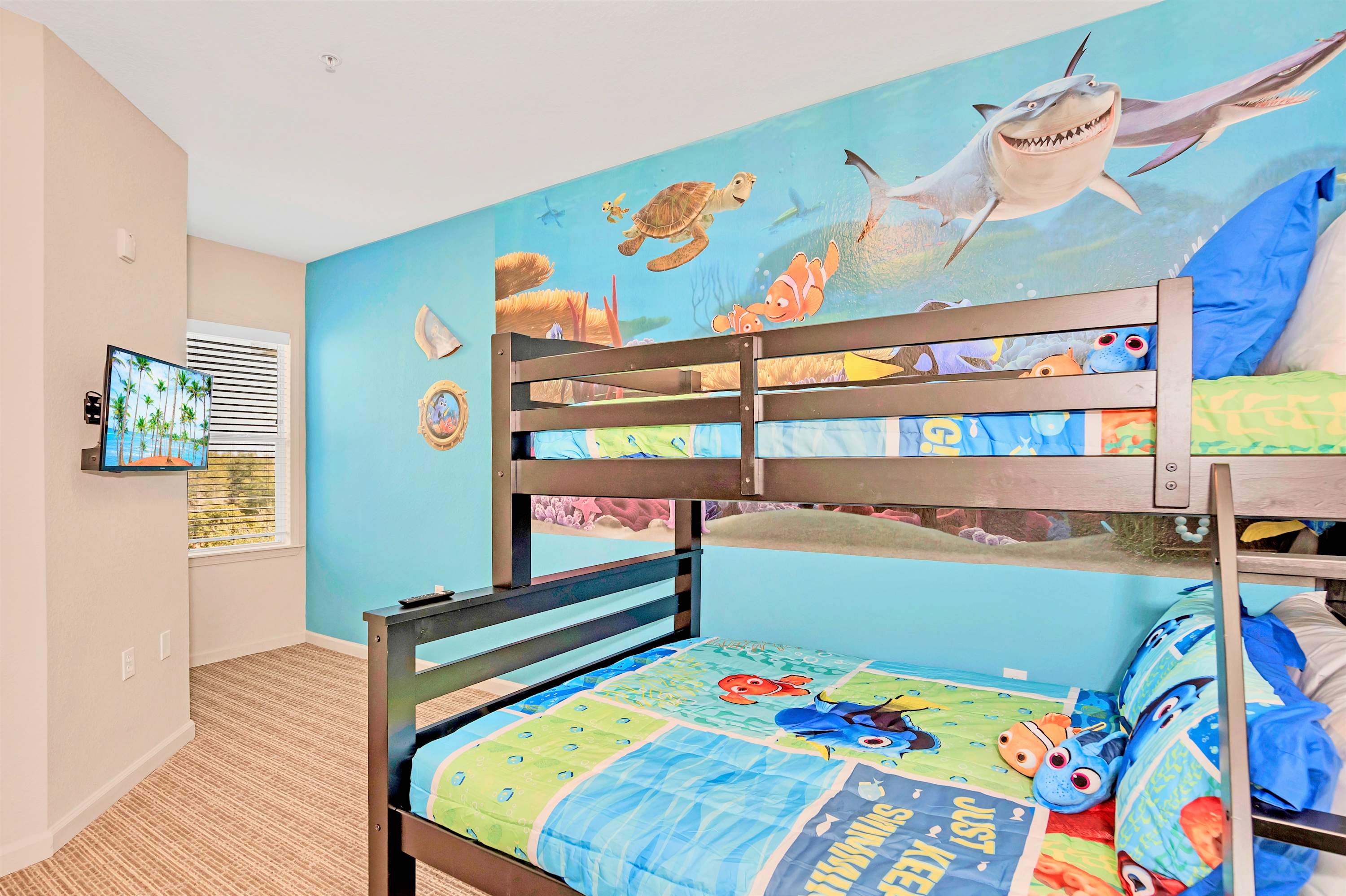 Another view of the kids' bedroom with a dark wood bunk bed, a vibrant Finding Nemo mural, and a wall-mounted TV near a window with blinds.
