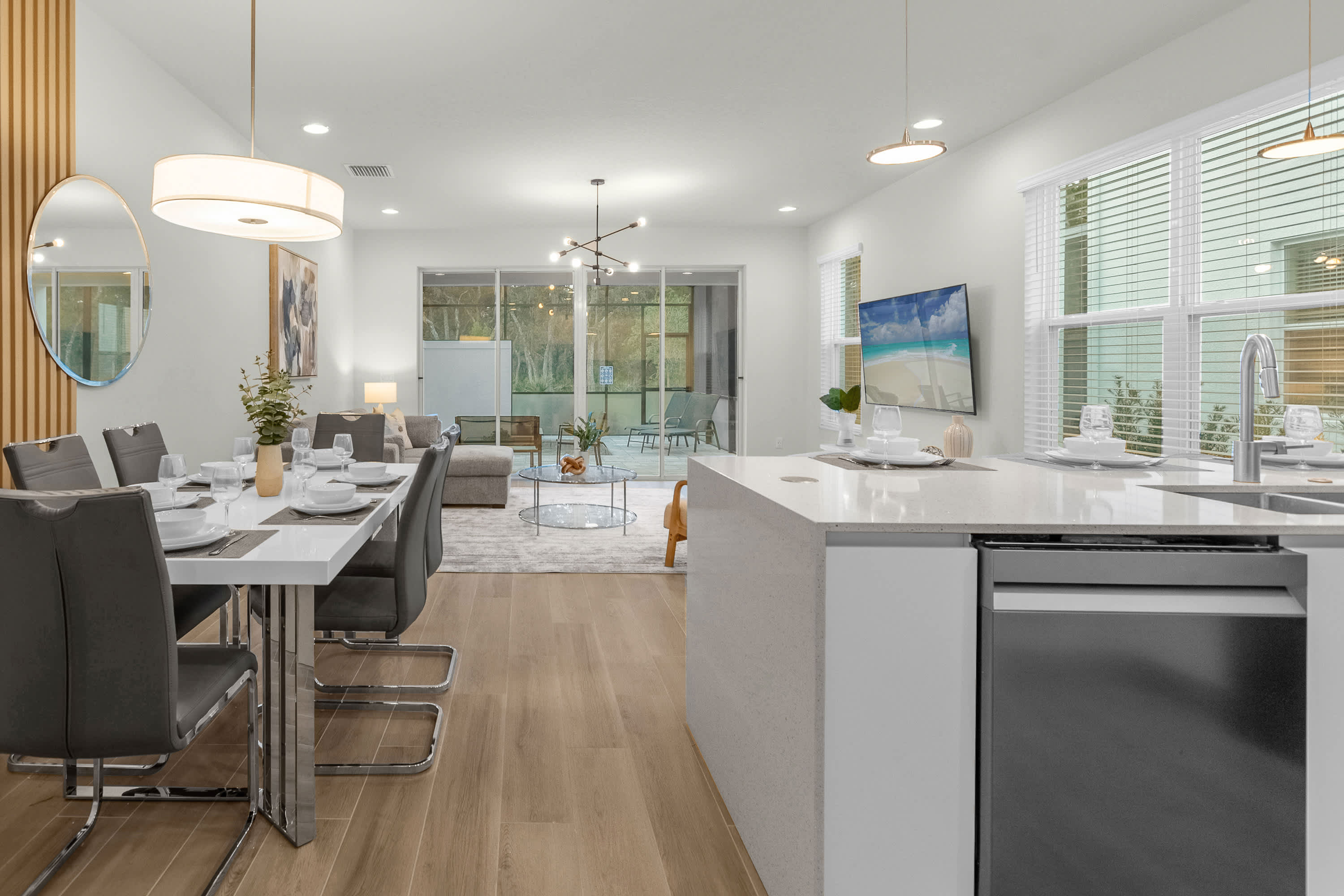 Spacious open-concept living area combining a modern kitchen island, a dining space with a white table, and a living room furnished with a sofa and a wall-mounted TV.