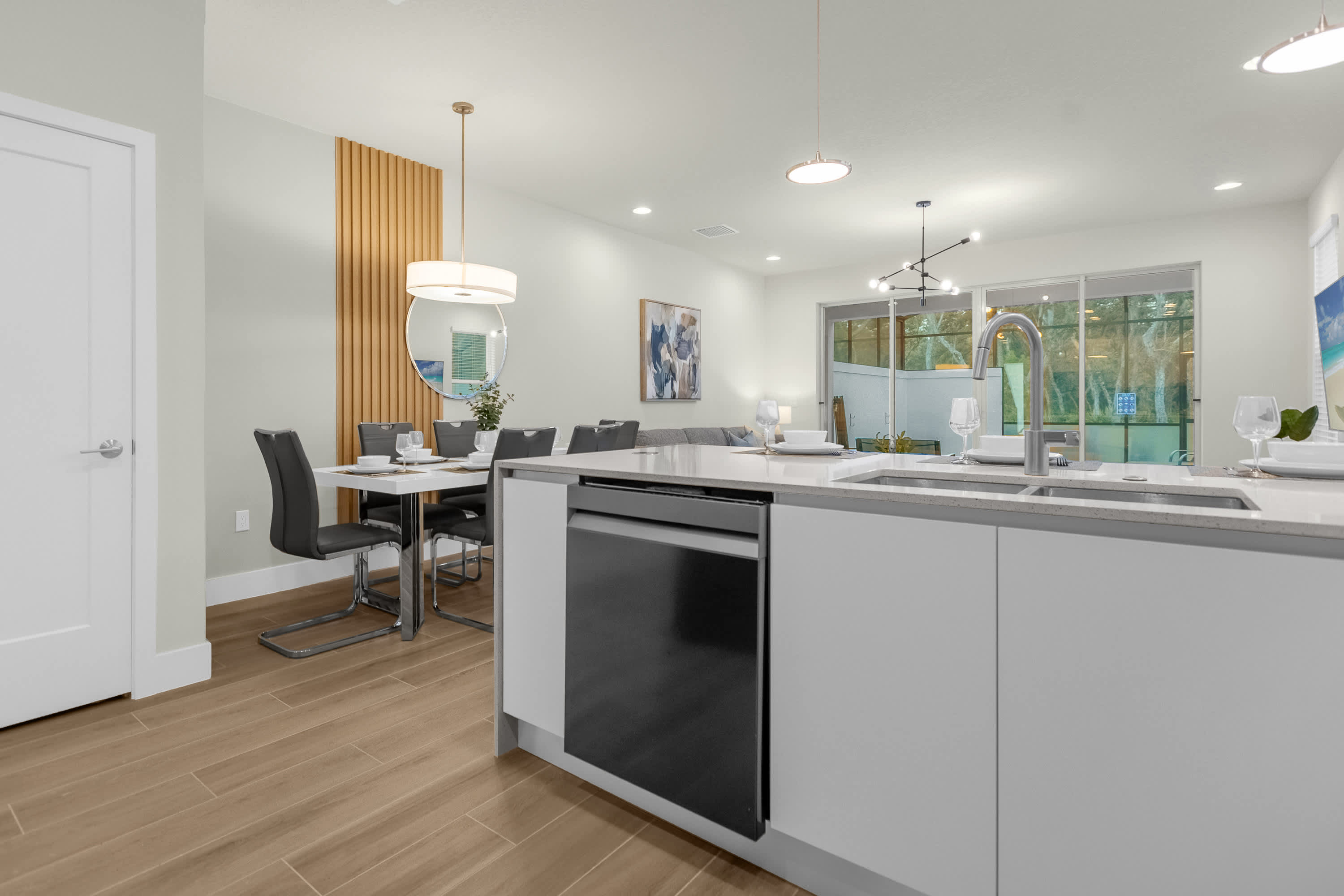 Modern open-concept kitchen featuring a light gray island with a black dishwasher and stainless steel sink, overlooking a dining area with a white table and dark chairs.