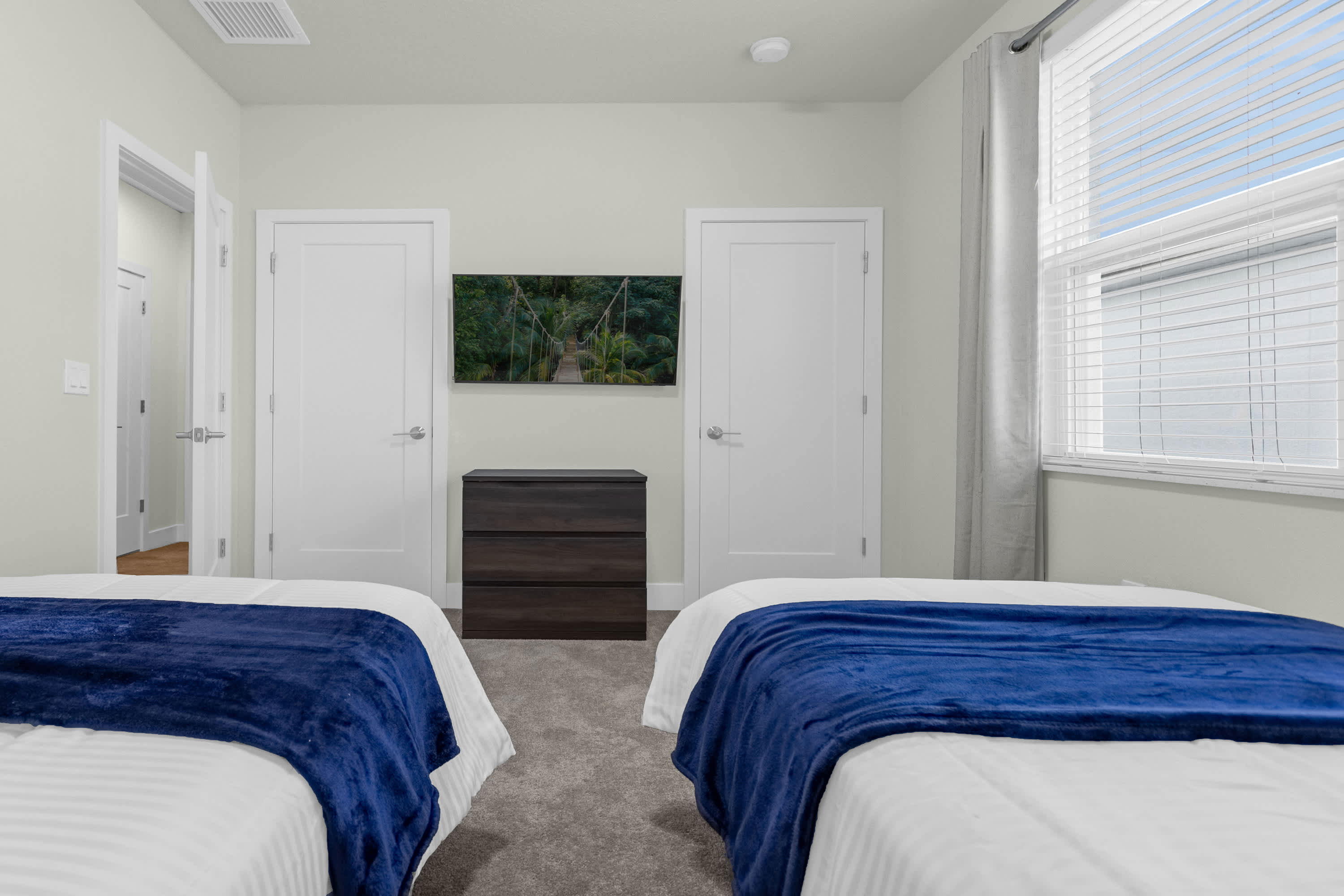 Another view of the kids' bedroom showcasing two twin beds, a dark wood dresser positioned between two white doors, and a wall-mounted TV.