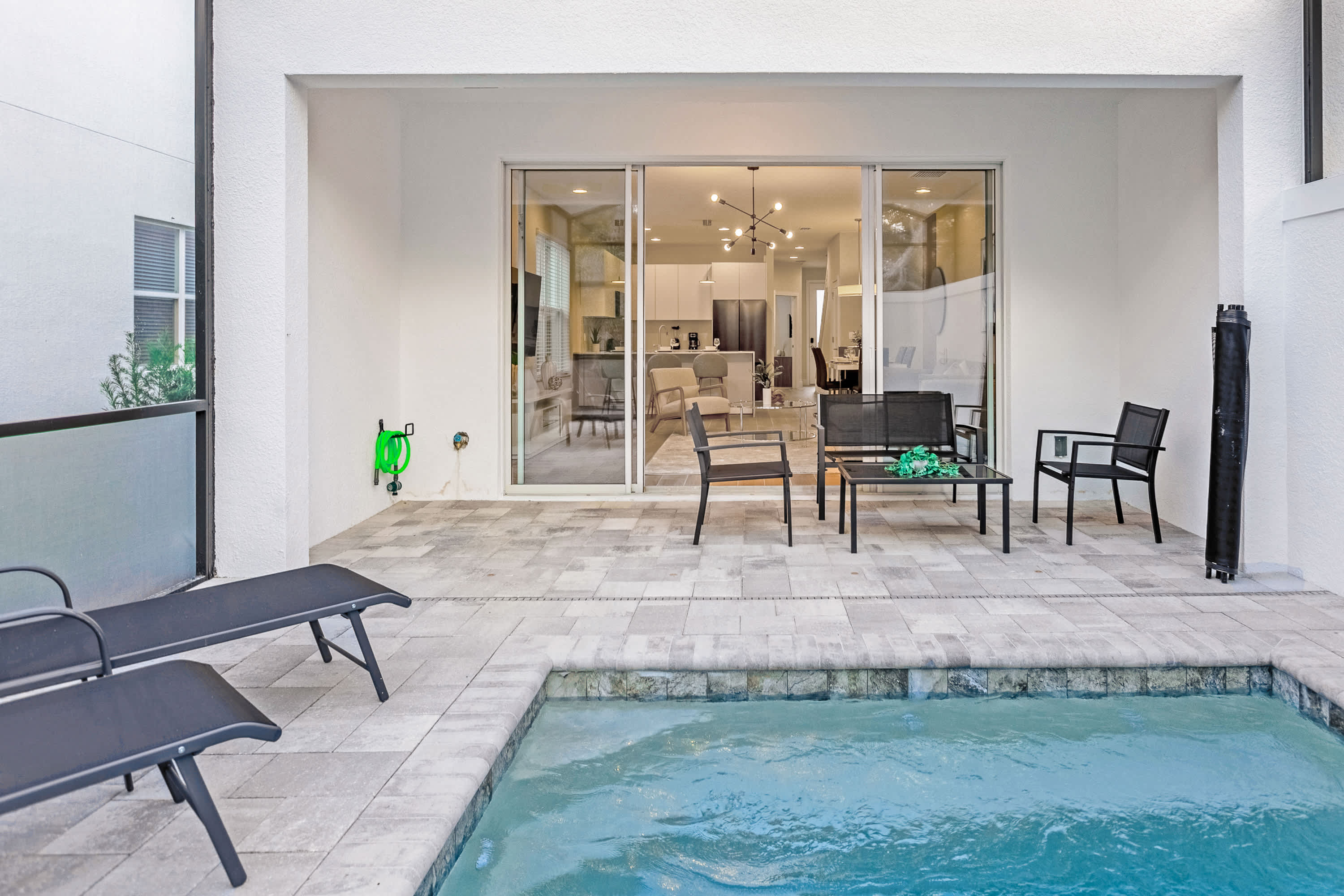 View of the outdoor patio and private pool area, showing the sliding glass doors leading into the main living space. The patio features light gray pavers, a small pool, and an outdoor seating arrangement with a table and chairs.