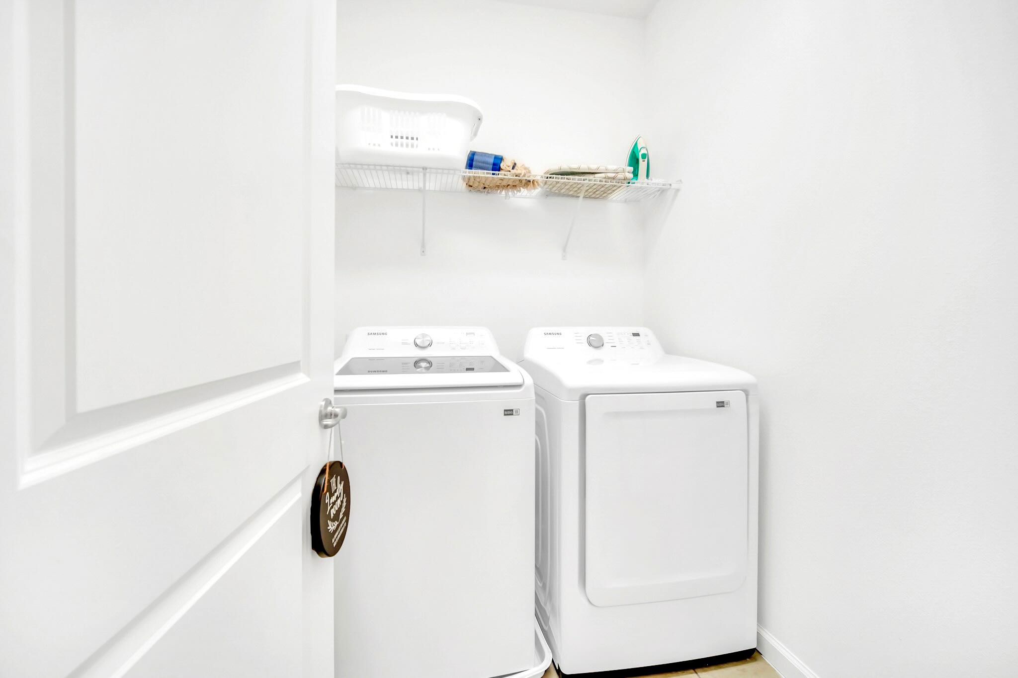 A dedicated laundry closet featuring a top-loading washing machine and a front-loading dryer, with a wire shelf above holding laundry essentials.
