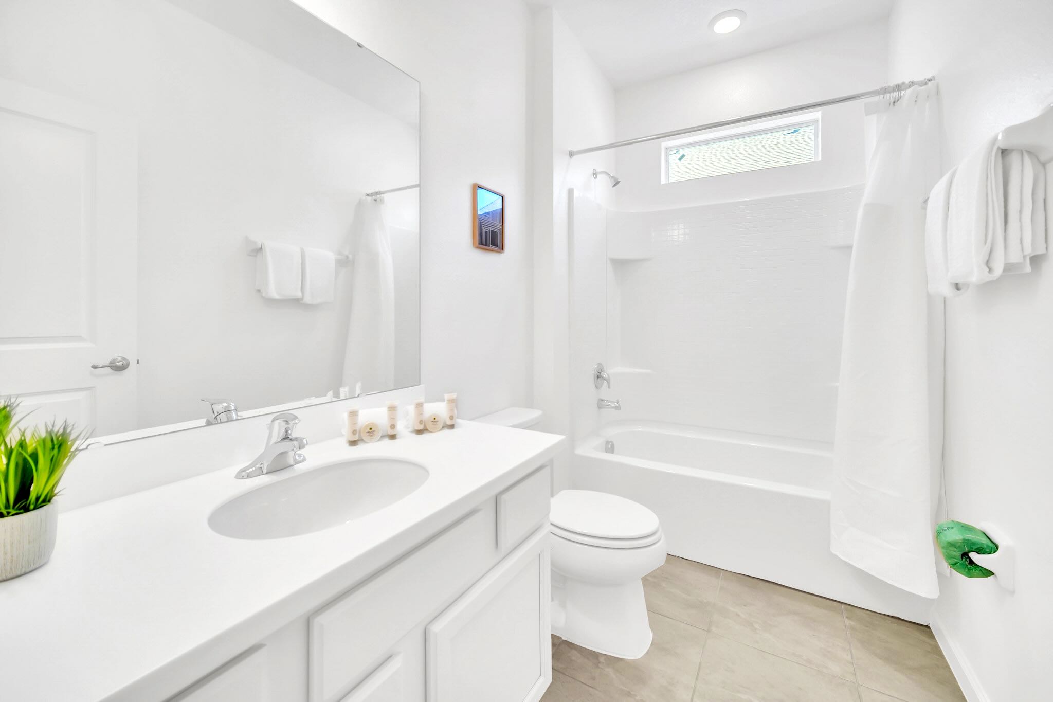 A bright, clean white bathroom featuring a single vanity with a white countertop, a large mirror, and a shower/tub combination with white subway tile surround.