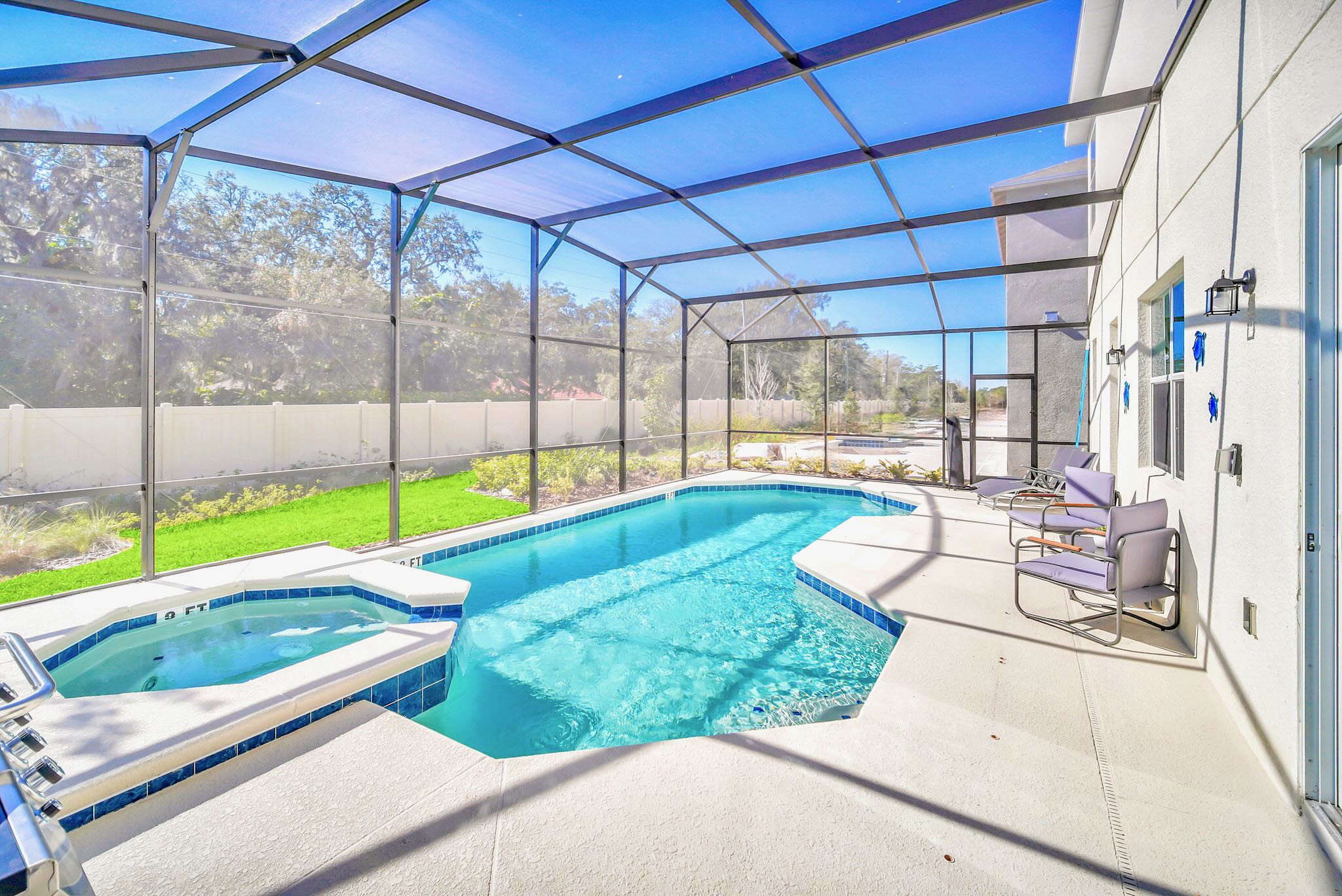 Expansive screened-in pool deck featuring a sparkling blue swimming pool with an integrated hot tub, surrounded by a spacious concrete patio and views of a grassy backyard.