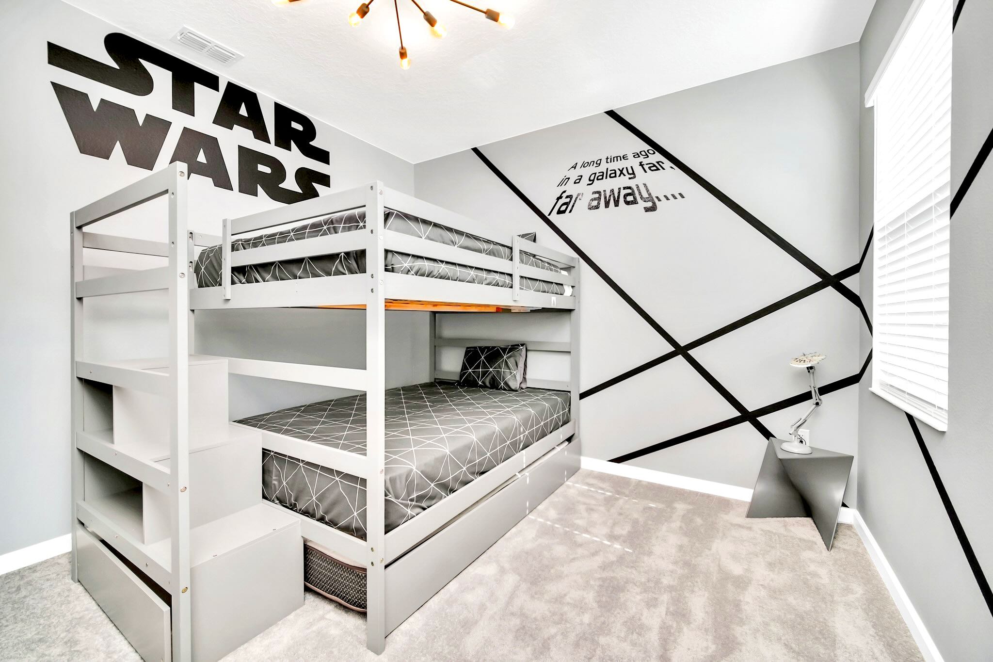 A modern Star Wars themed bedroom featuring a gray bunk bed with geometric patterned bedding, and a striking black and white wall mural with the Star Wars logo and text.